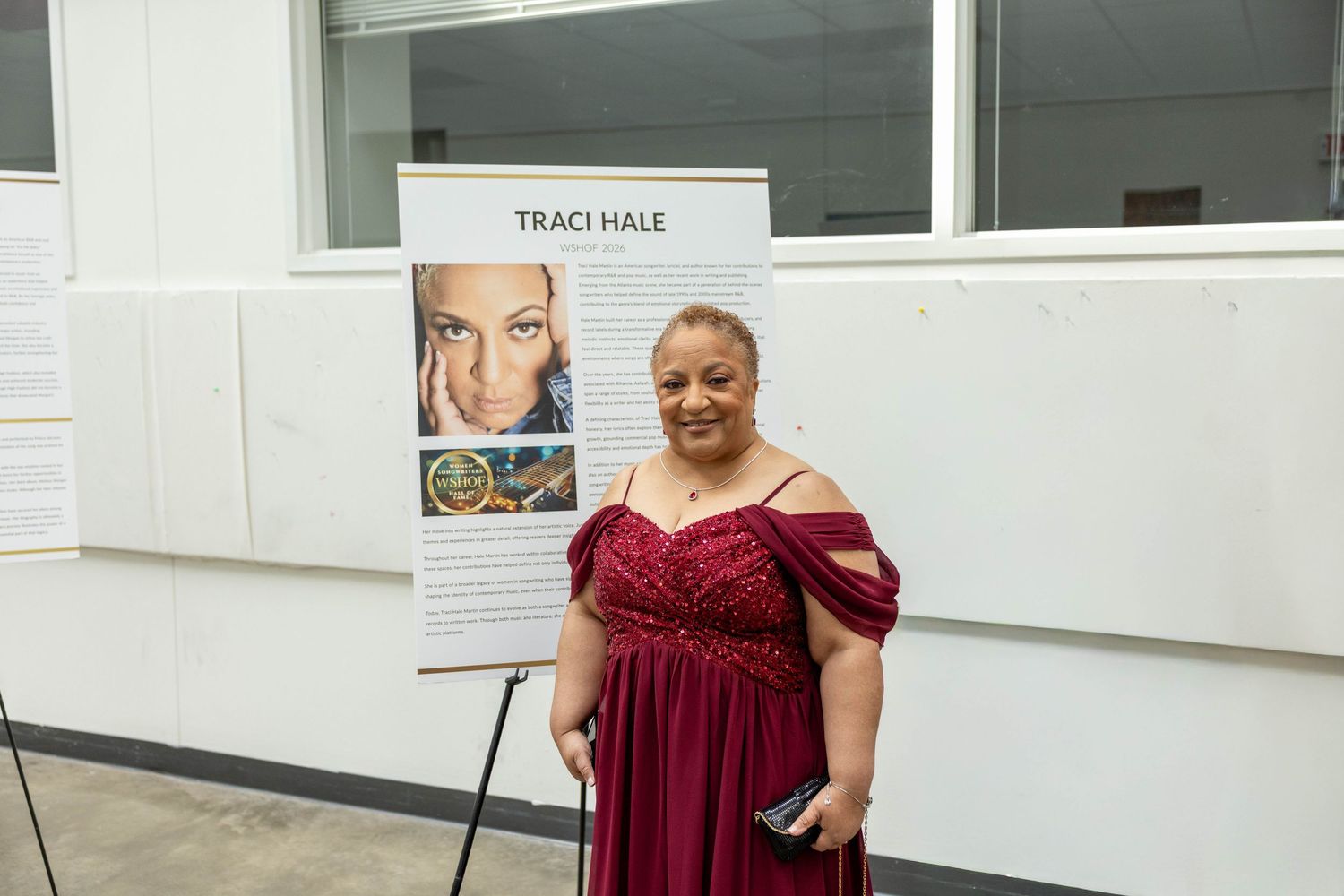Woman in red gown stands beside a Traci Hale recognition display board at a formal event.