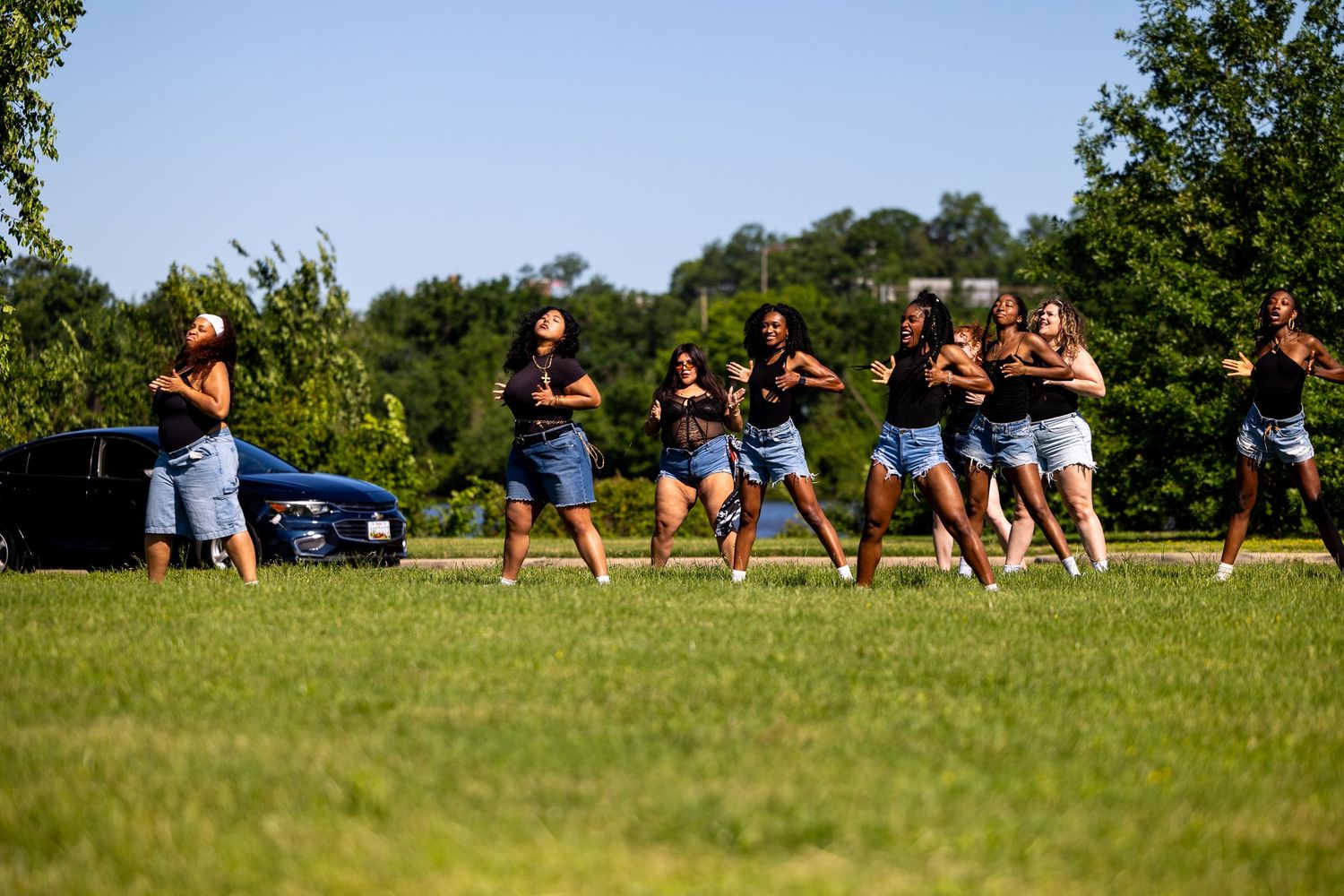 Group of women performing a synchronized dance routine outdoors on green grass during a sunny day.
