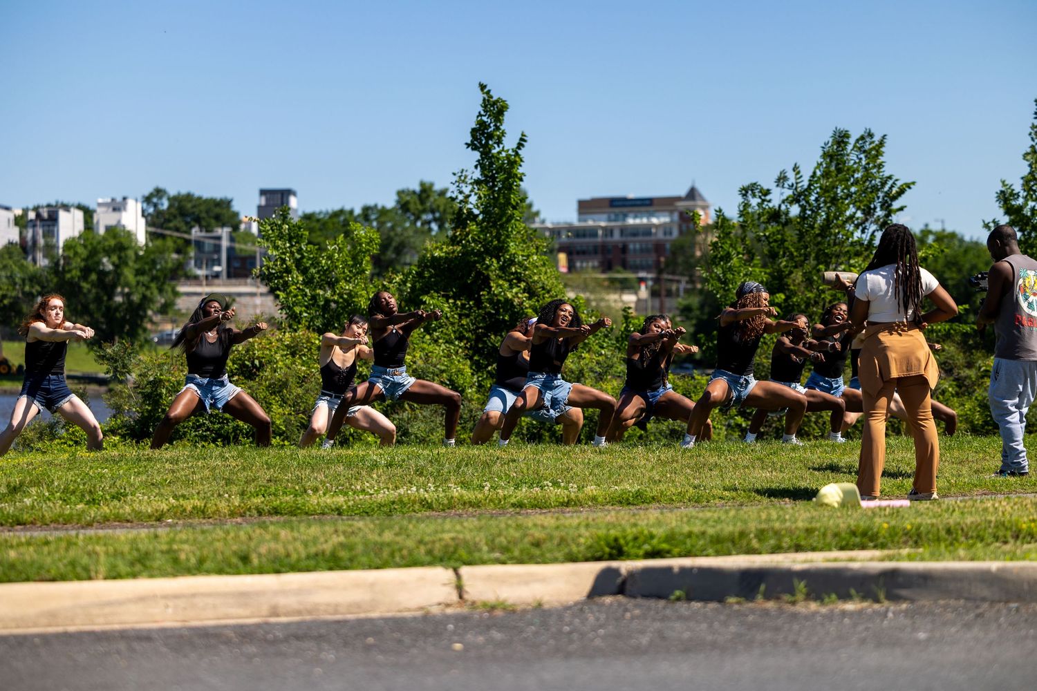 Group of people performing a synchronized outdoor dance routine on a grassy area on a sunny day.