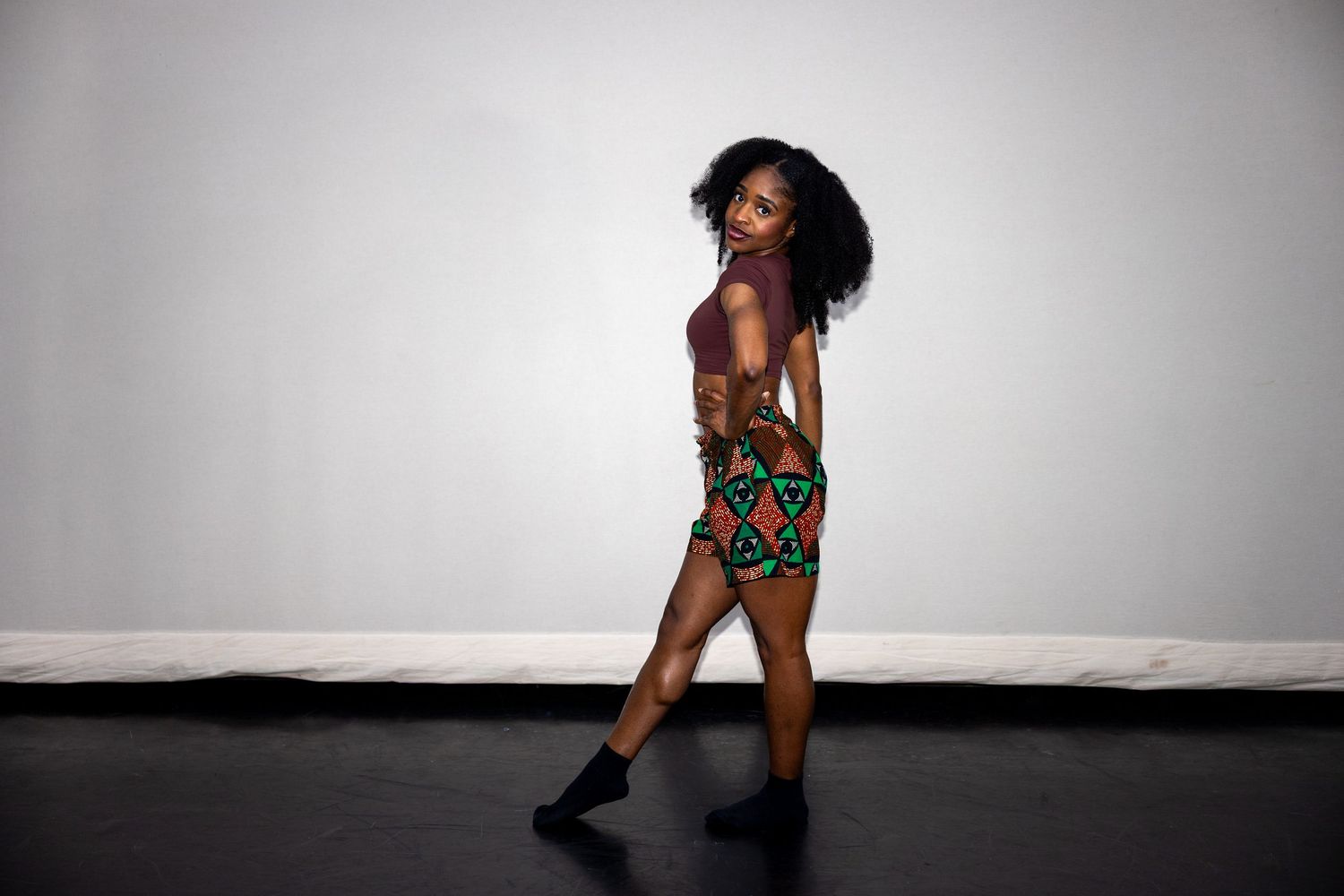 Woman in colorful African print mini dress walking on black stage floor.