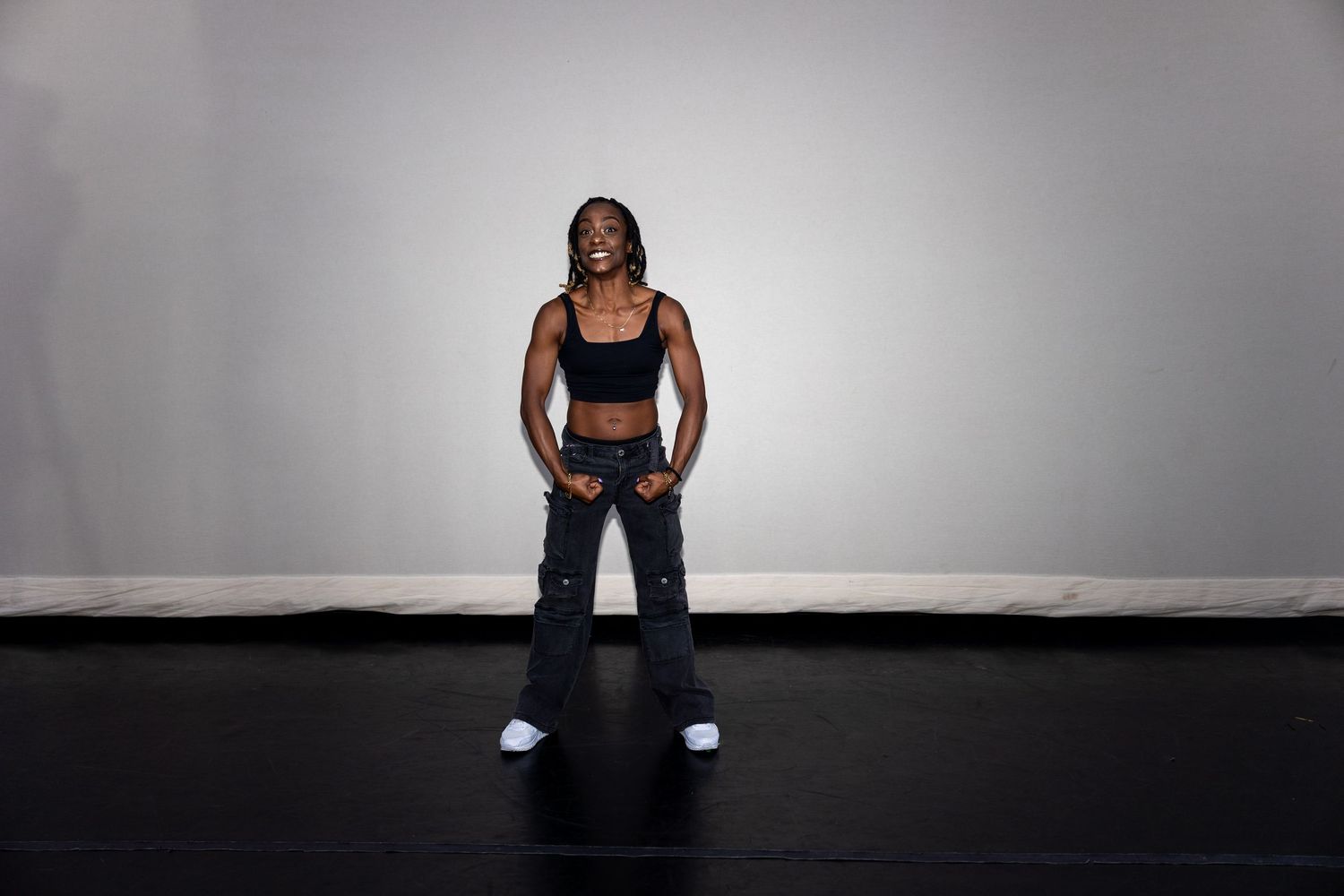Woman in black sports bra and flared pants standing confidently with white sneakers against gray background.