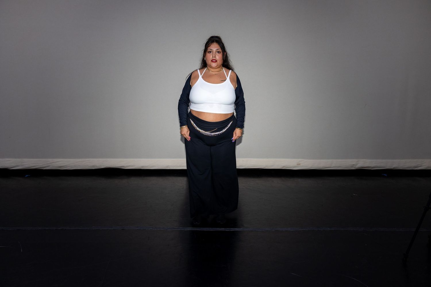Woman in white crop top, navy cardigan, and wide-leg pants stands confidently against a gray studio backdrop.