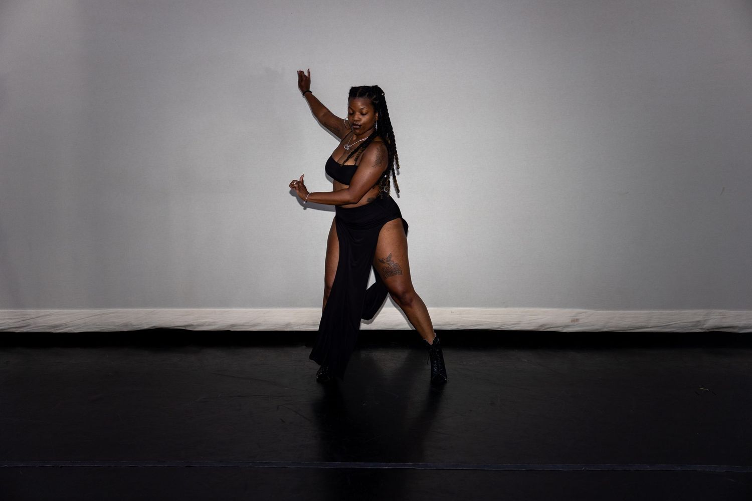 Graceful Black female dancer in black dress performing an elegant pose on a dark studio floor.