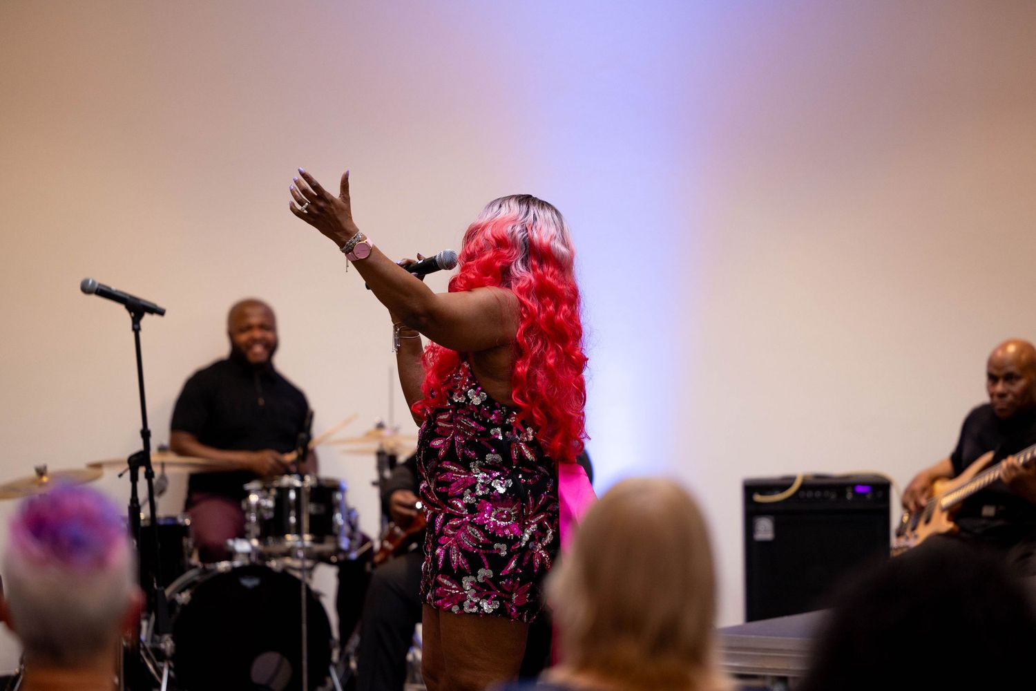 Performer with pink hair singing on stage with live band during energetic indoor concert event.