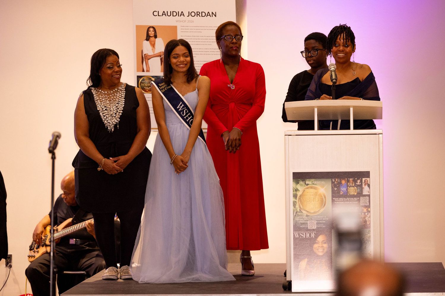 Four women standing together on stage at formal Claudia Jordan event.
