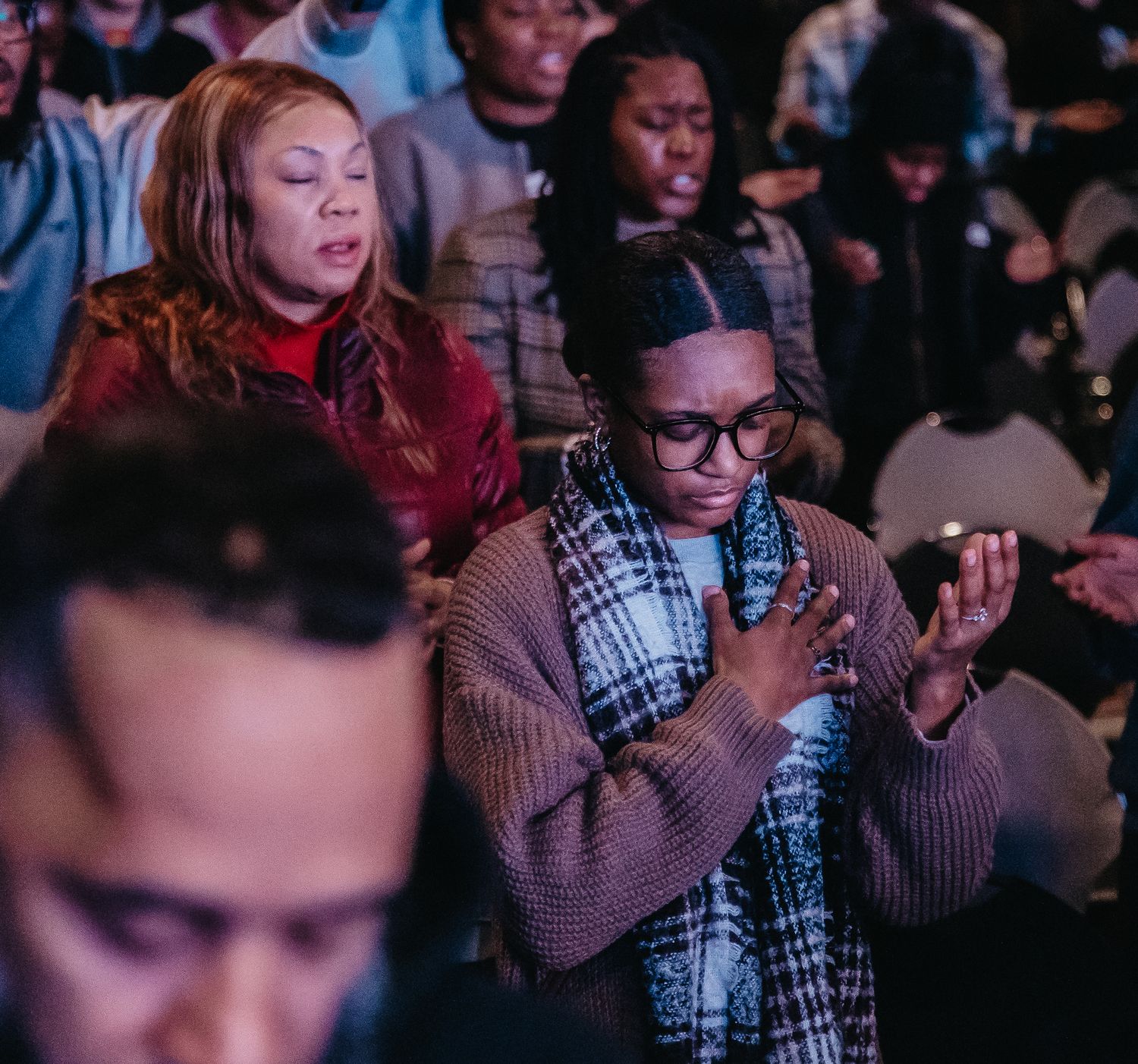 Audience members in a dark theater hold up glowing smartphones to record or take photos during a performance.