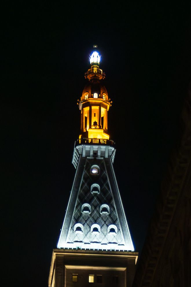 Art deco tower illuminated in gold and white light against dark night sky.