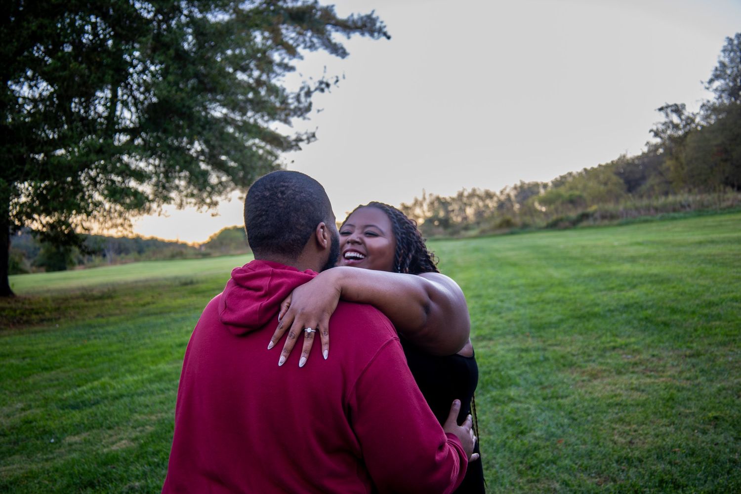 A couple embracing outdoors during sunset in a grassy field.
