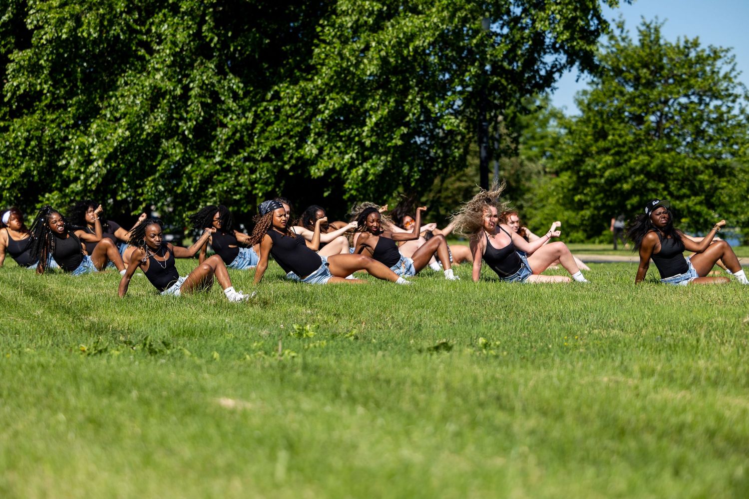 Group of young women exercising outdoors on green grass in a sunny park surrounded by trees.