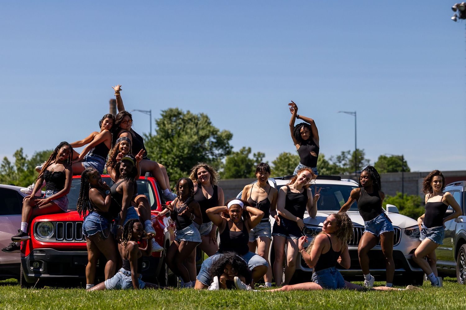 Group of young women posing together outdoors near cars on a sunny day, celebrating and having fun.