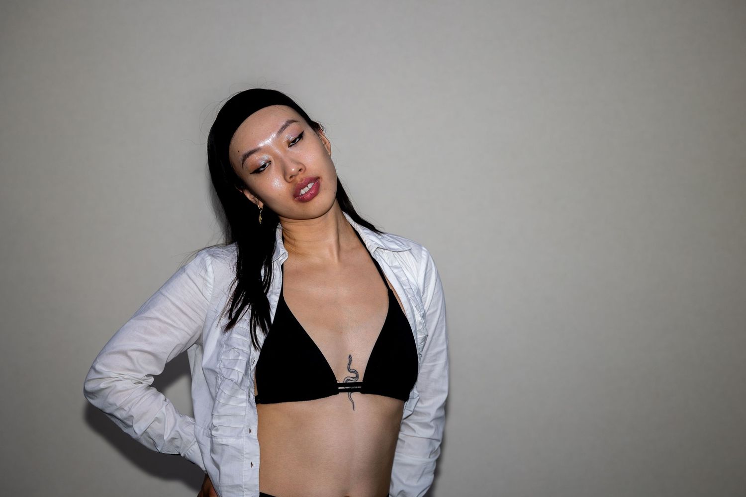 Woman in white jacket and black bikini top posing confidently against dark background.