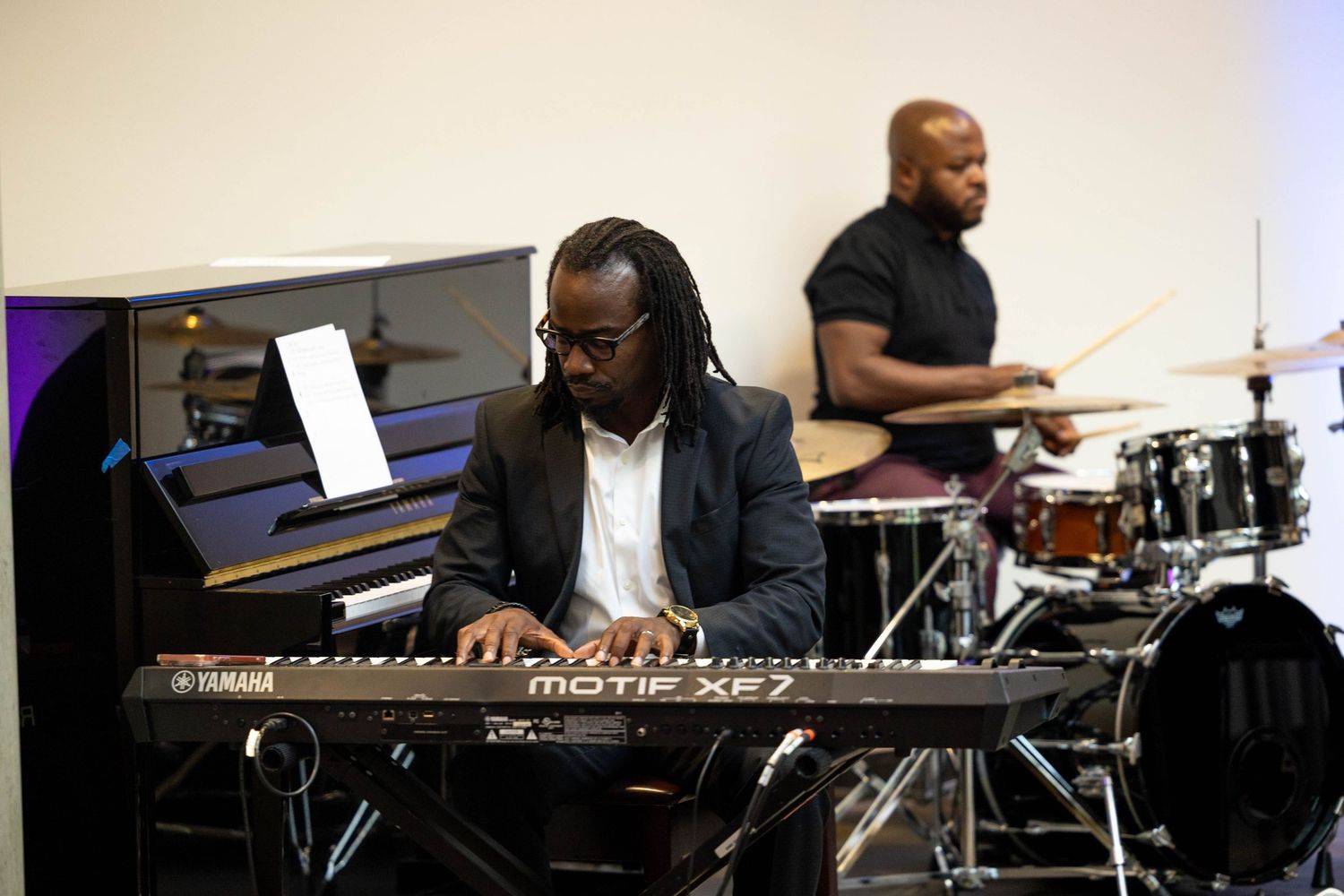Musician playing Yamaha Motif XF7 keyboard with drummer performing live on stage behind him.