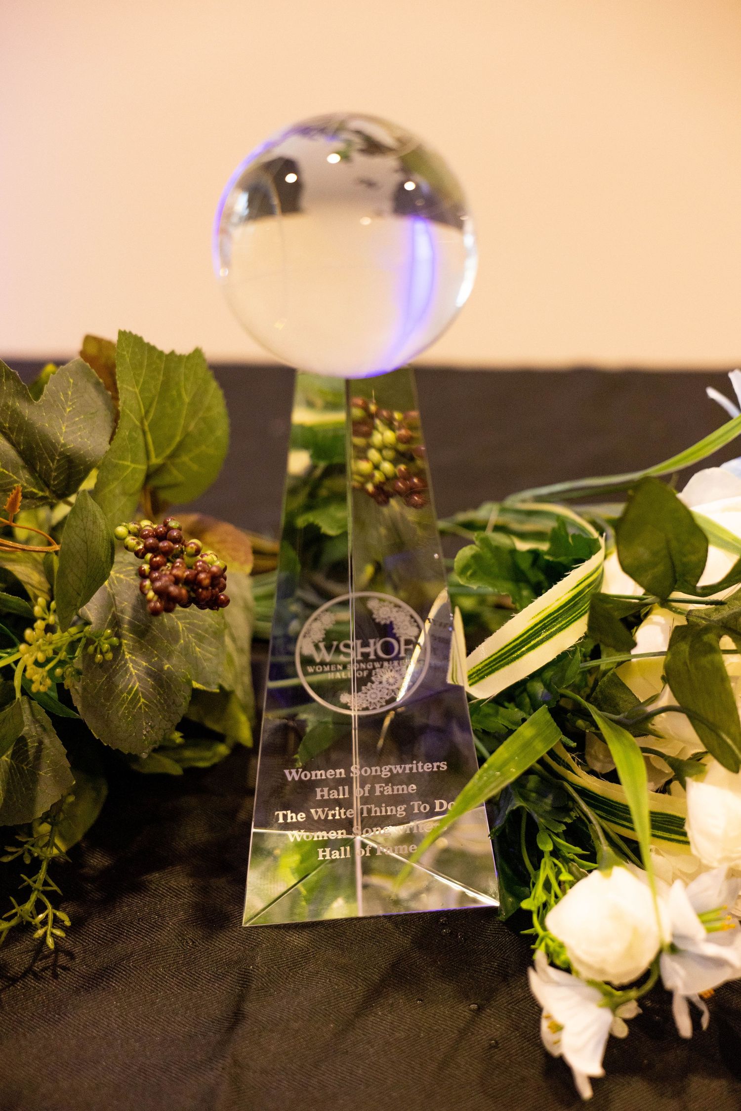 Women Songwriters Hall of Fame crystal globe trophy award displayed with white roses and greenery.