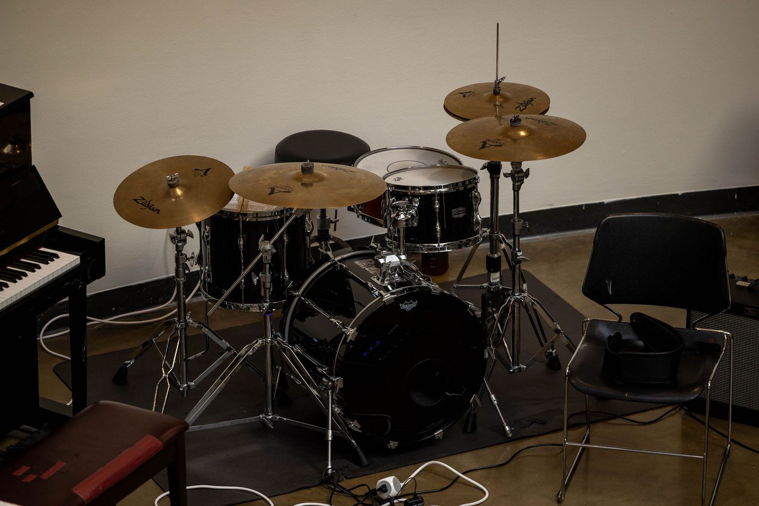 Black drum kit with cymbals set up in a practice room next to a piano.