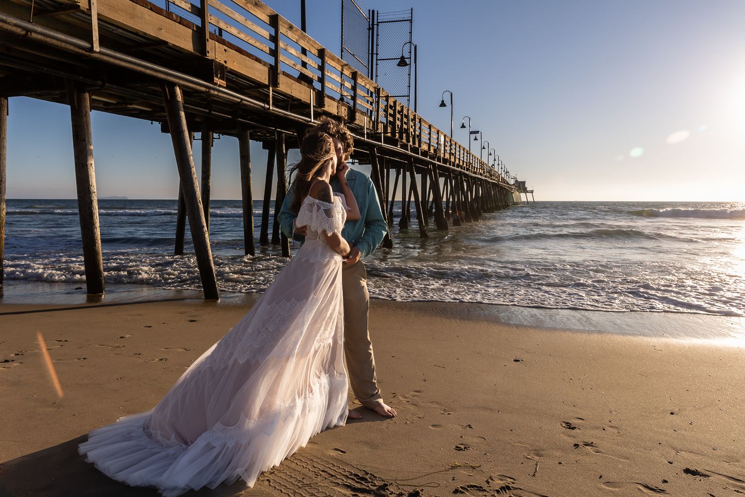 Romantic beach wedding photoshoot at sunset with bride in flowing white dress walking along wooden pier. traveling photographer, Arizona, CA