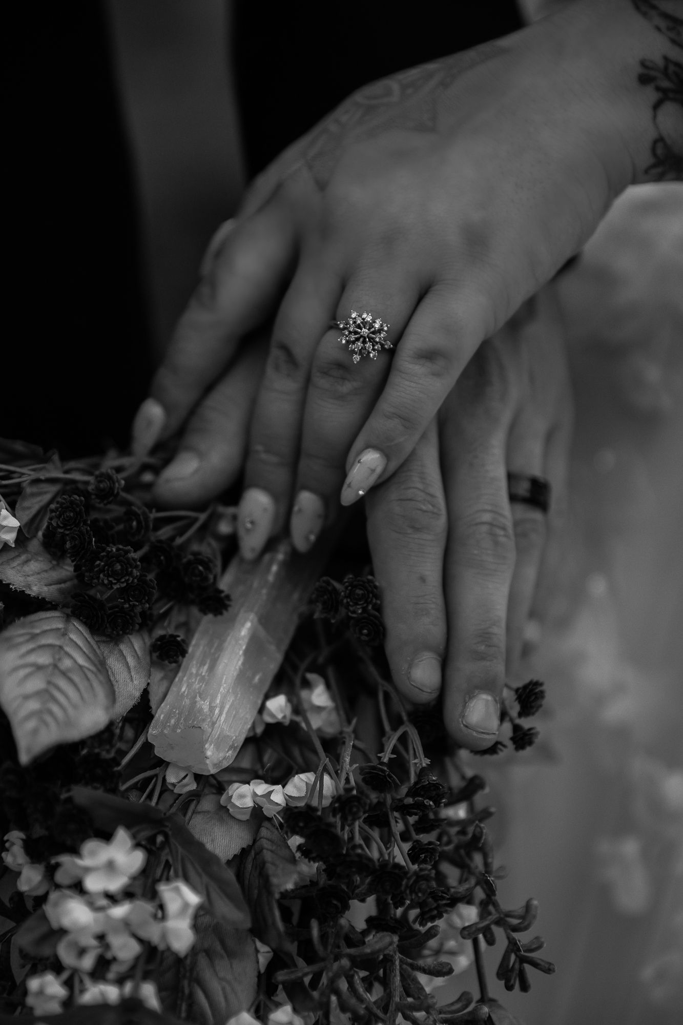 Close-up black and white photo of hands wearing rings while arranging flowers and foliage. wedding details wedding photography Arizona
