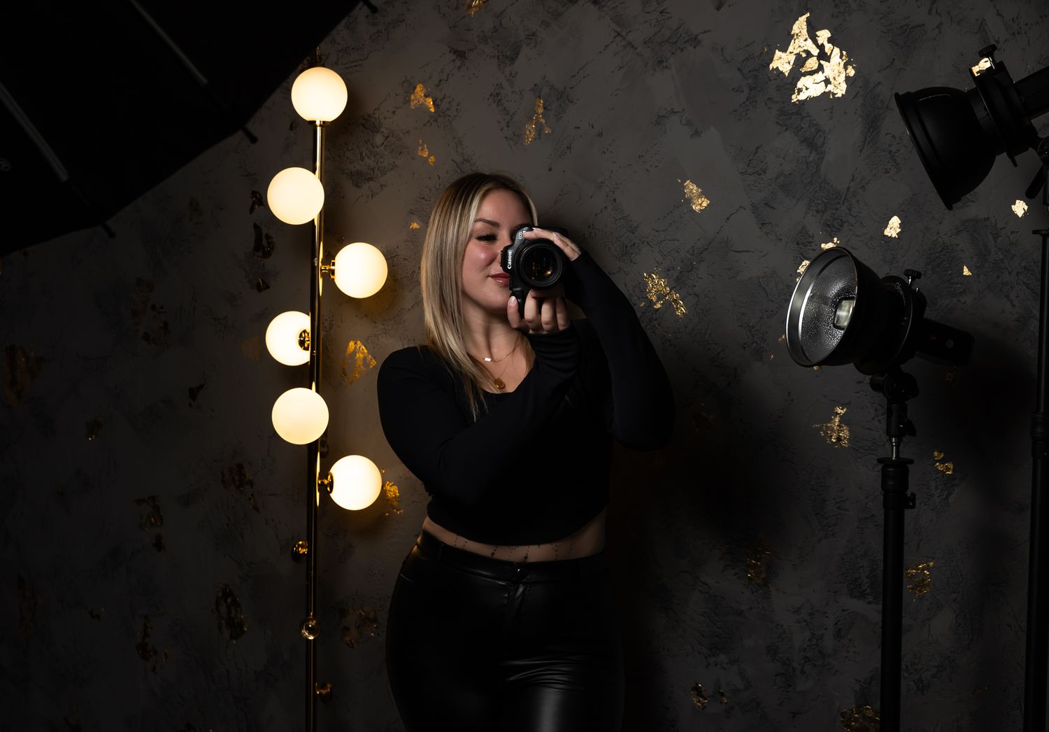 A person's hand holds a black camera against a dark background with glowing circular bokeh lights.