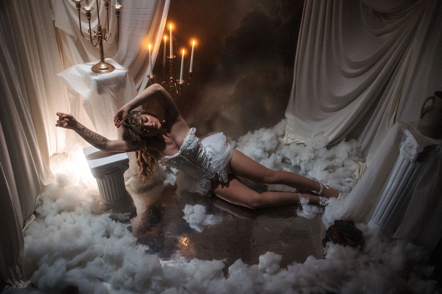 A person lies on a cloud-like bed surrounded by white fluffy pillows and soft lighting in a dreamy atmosphere.
