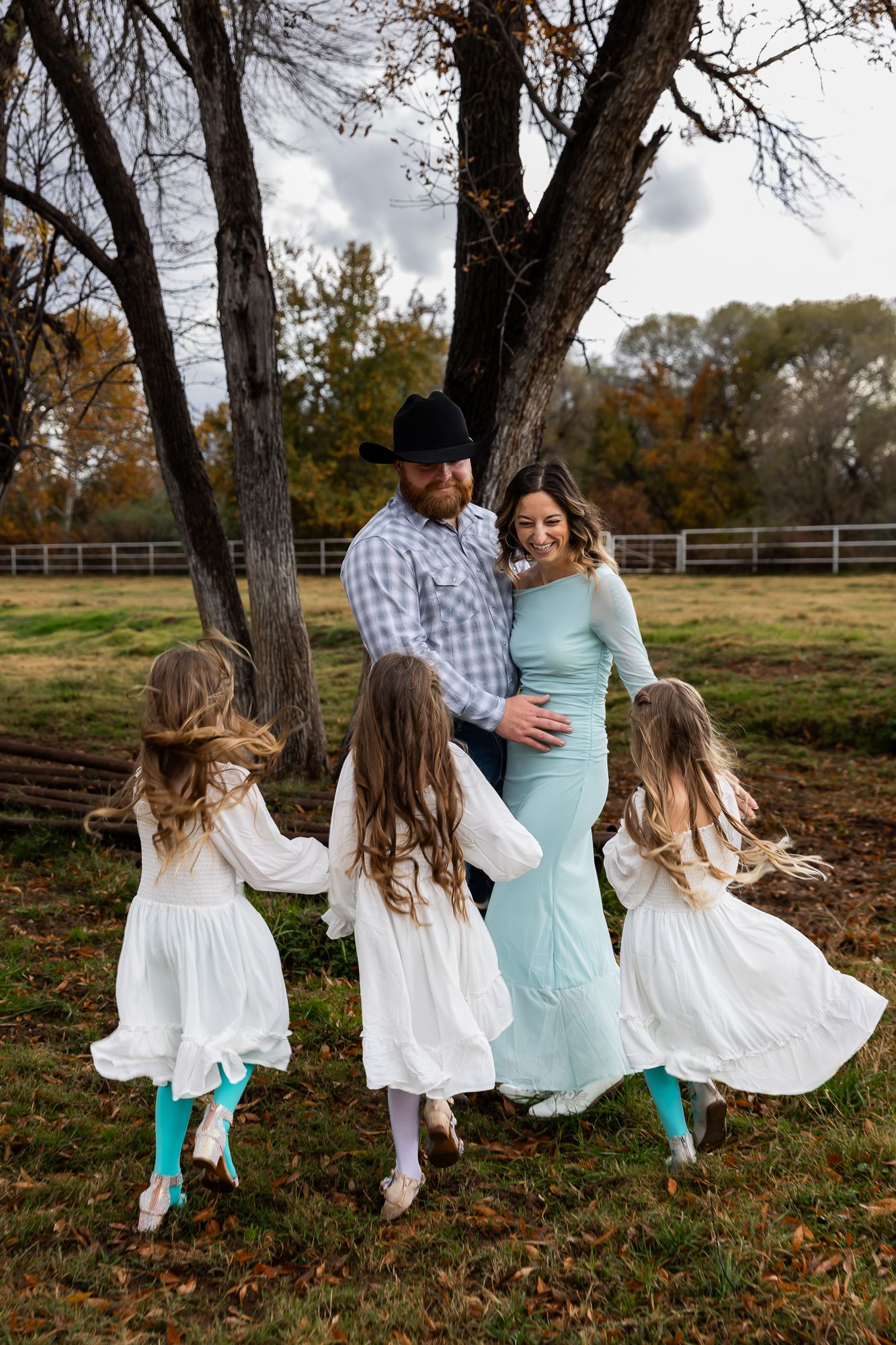 Family dancing together outdoors among autumn trees wearing turquoise and white.