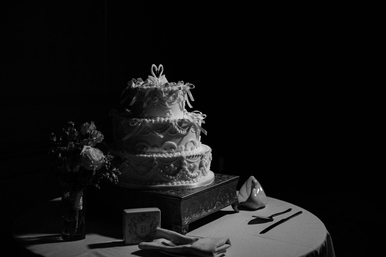 Black and white photograph of an elegant tiered wedding cake with floral decorations on a table with place settings.