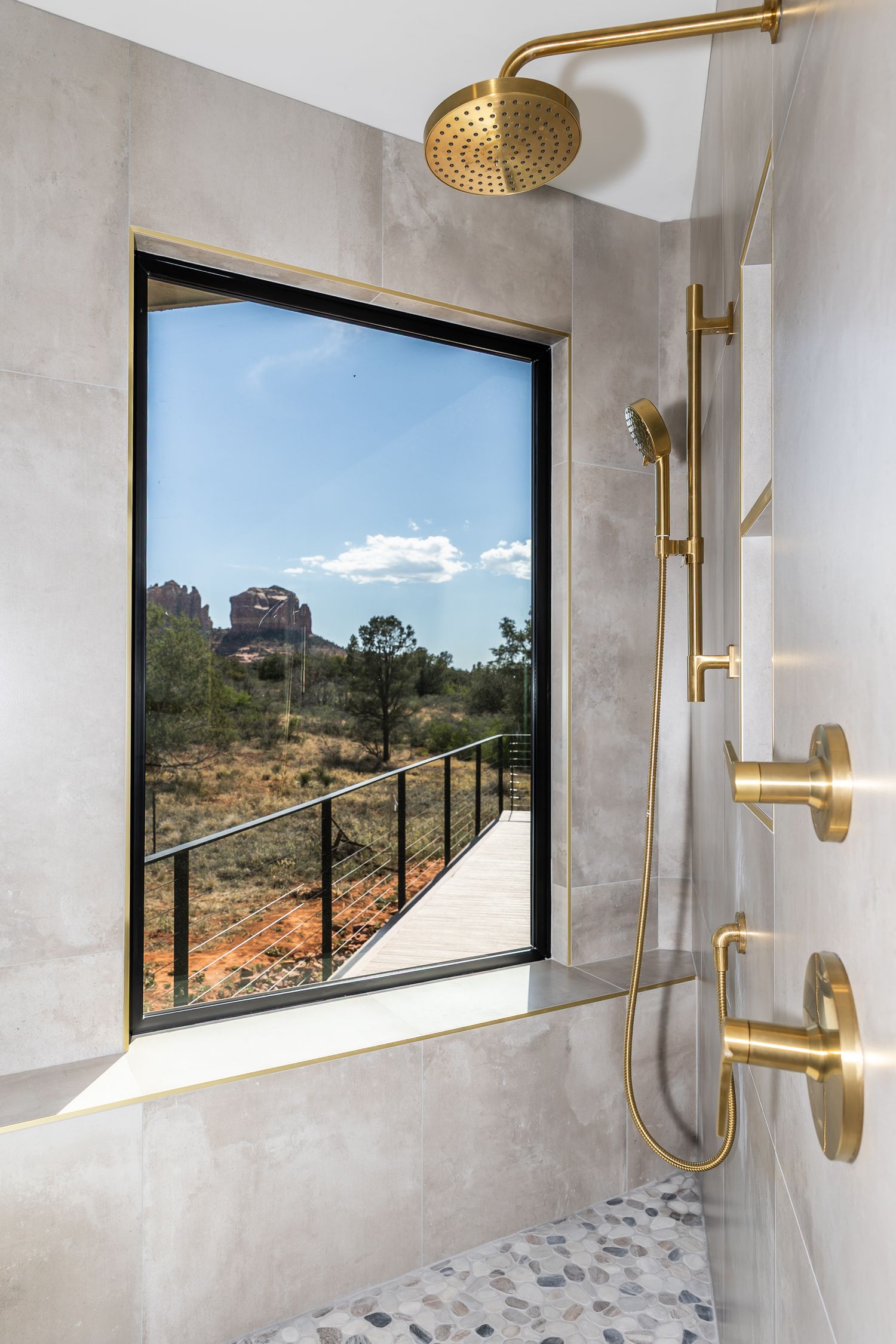 Modern bathroom with concrete walls features large windows offering desert views and gold-finished fixtures and shower head. Sedona az