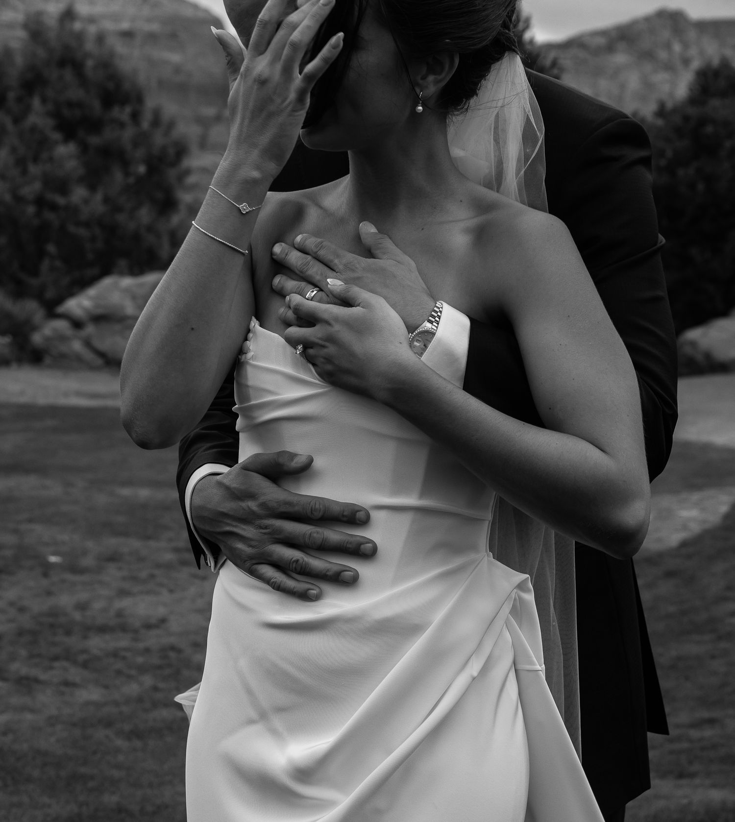 A couple in formal wedding attire embrace during an outdoor photo session with mountains in the background.