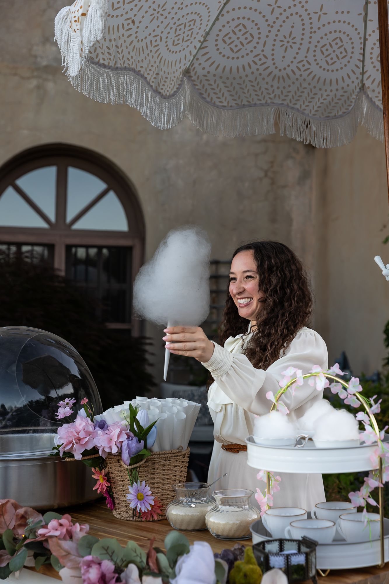 Woman enjoying tea and treats at an elegant table setting with lace decor.