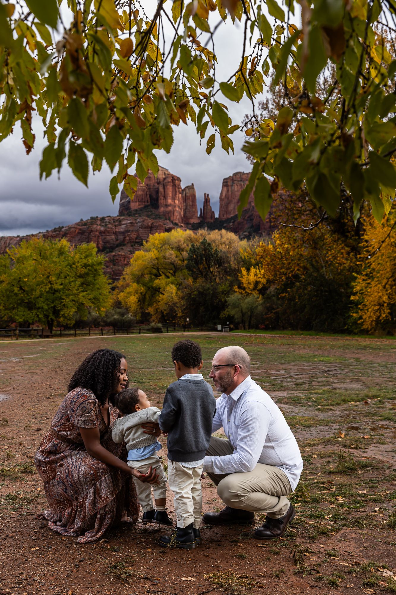 A group sits on the ground with red rock formations and autumn trees visible in the background at Cathedral Rock in Sedona.