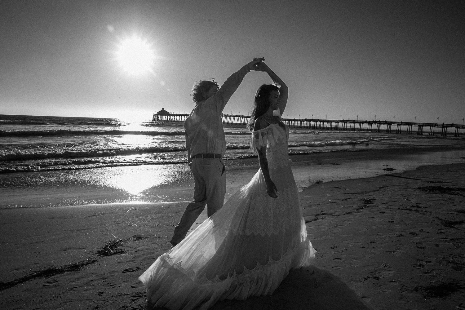 Silhouetted figures dance on a beach at sunset with a pier in the background. California elopement