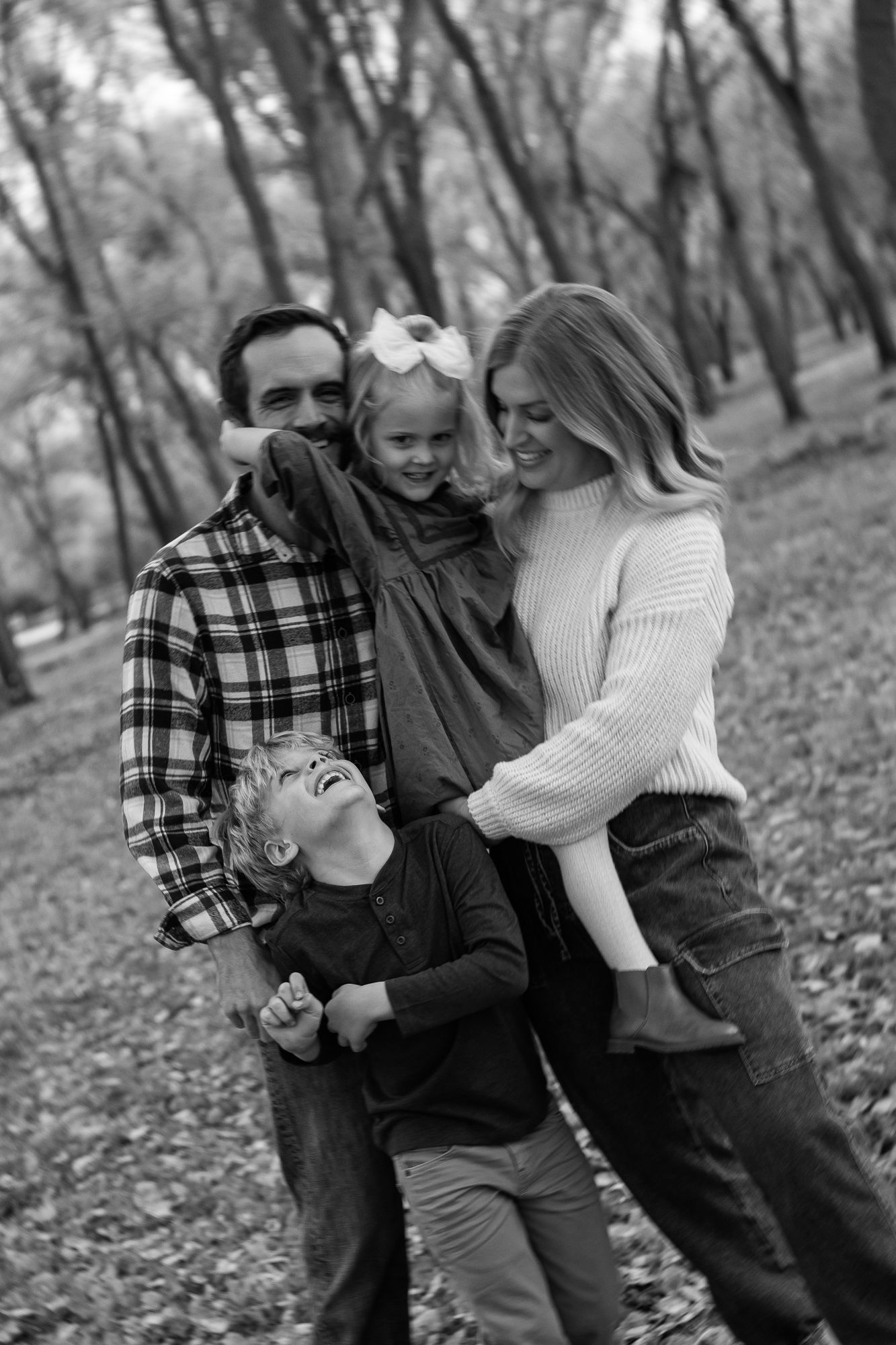 A family shares joyful laughter together during an autumn photoshoot in a wooded area.
