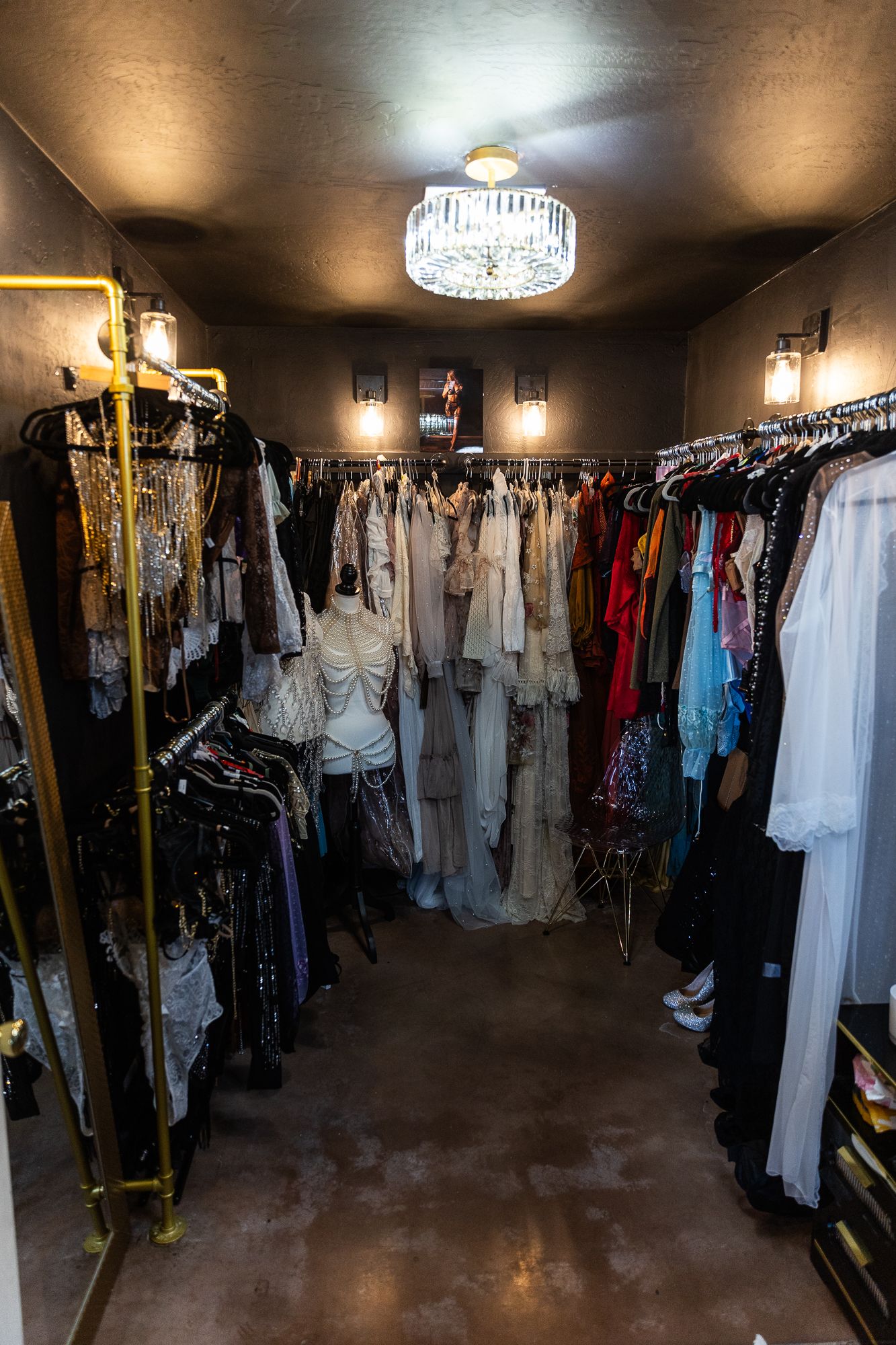 A large walk-in closet with racks of formal dresses and clothing illuminated by an elegant crystal chandelier. cottonwood photography studio
