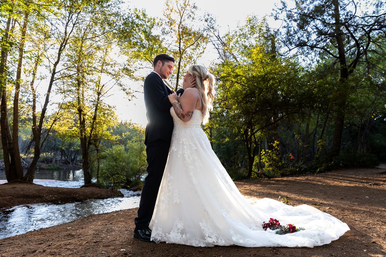 A couple in wedding attire shares a romantic moment in a sunlit outdoor setting with autumn trees in the background. Sedona photographer, AZ
