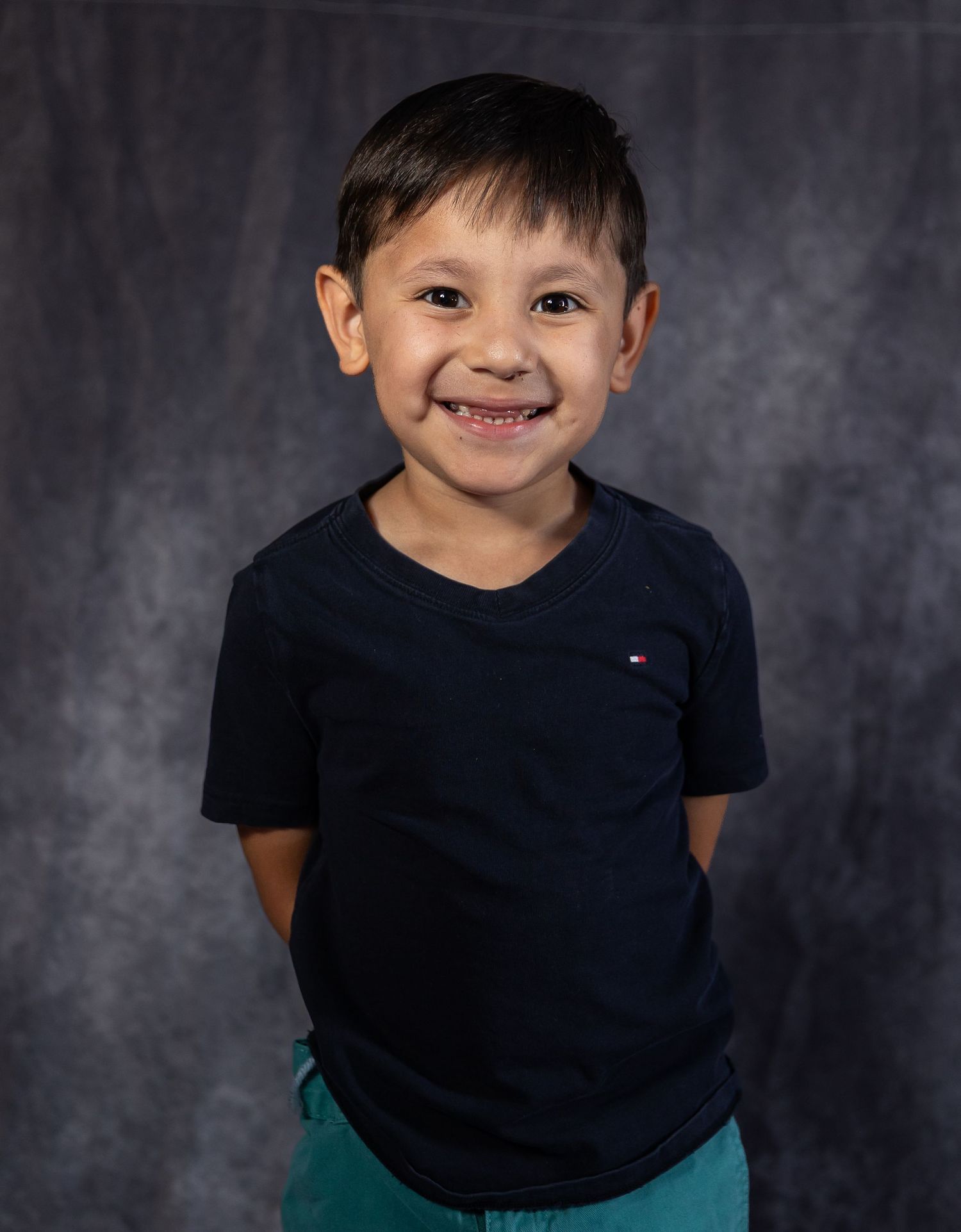 Smiling young boy in navy Tommy Hilfiger t-shirt and teal shorts posing for a school portrait photo.