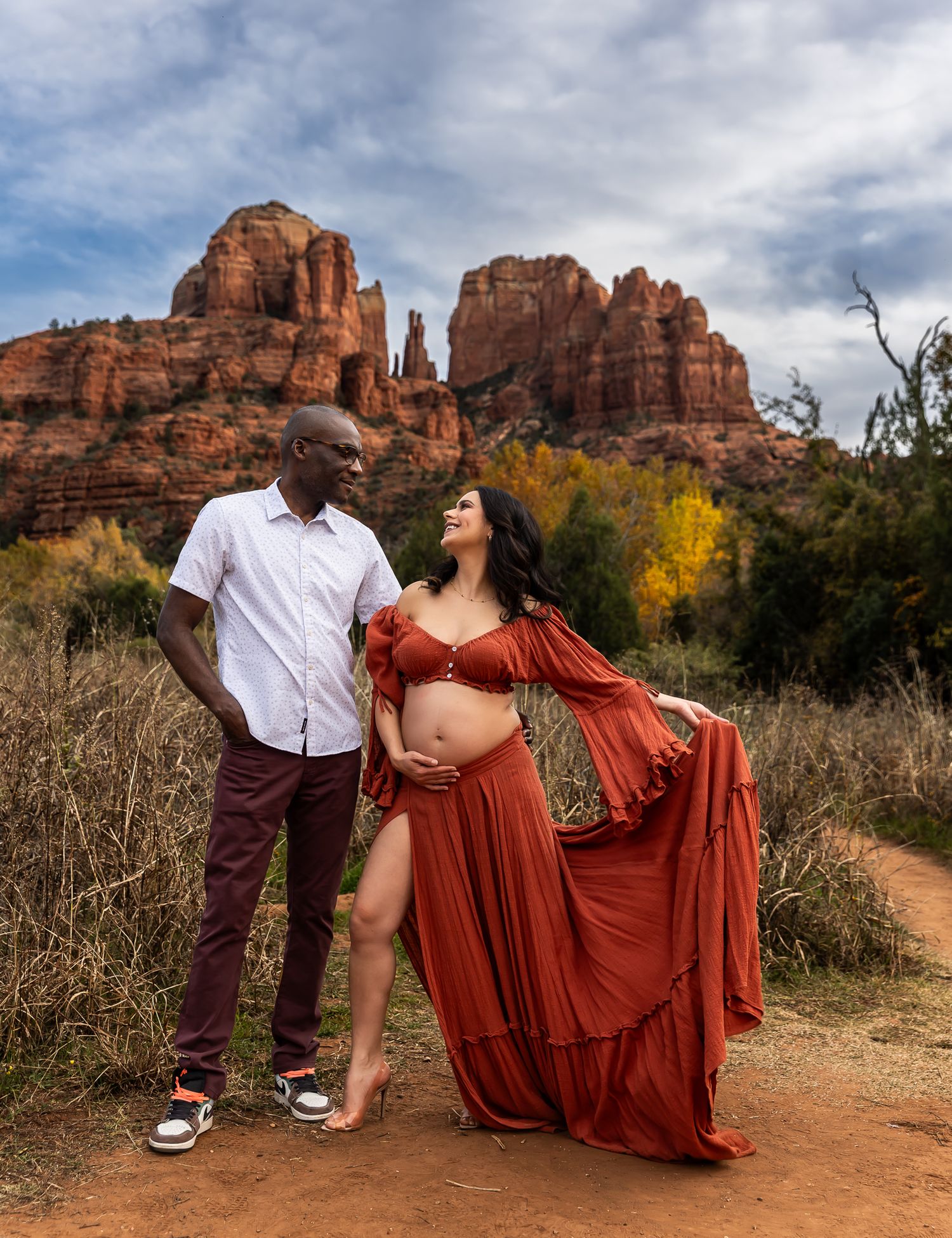 A romantic couple poses together against stunning red rock formations in Sedona with dramatic cloudy skies.