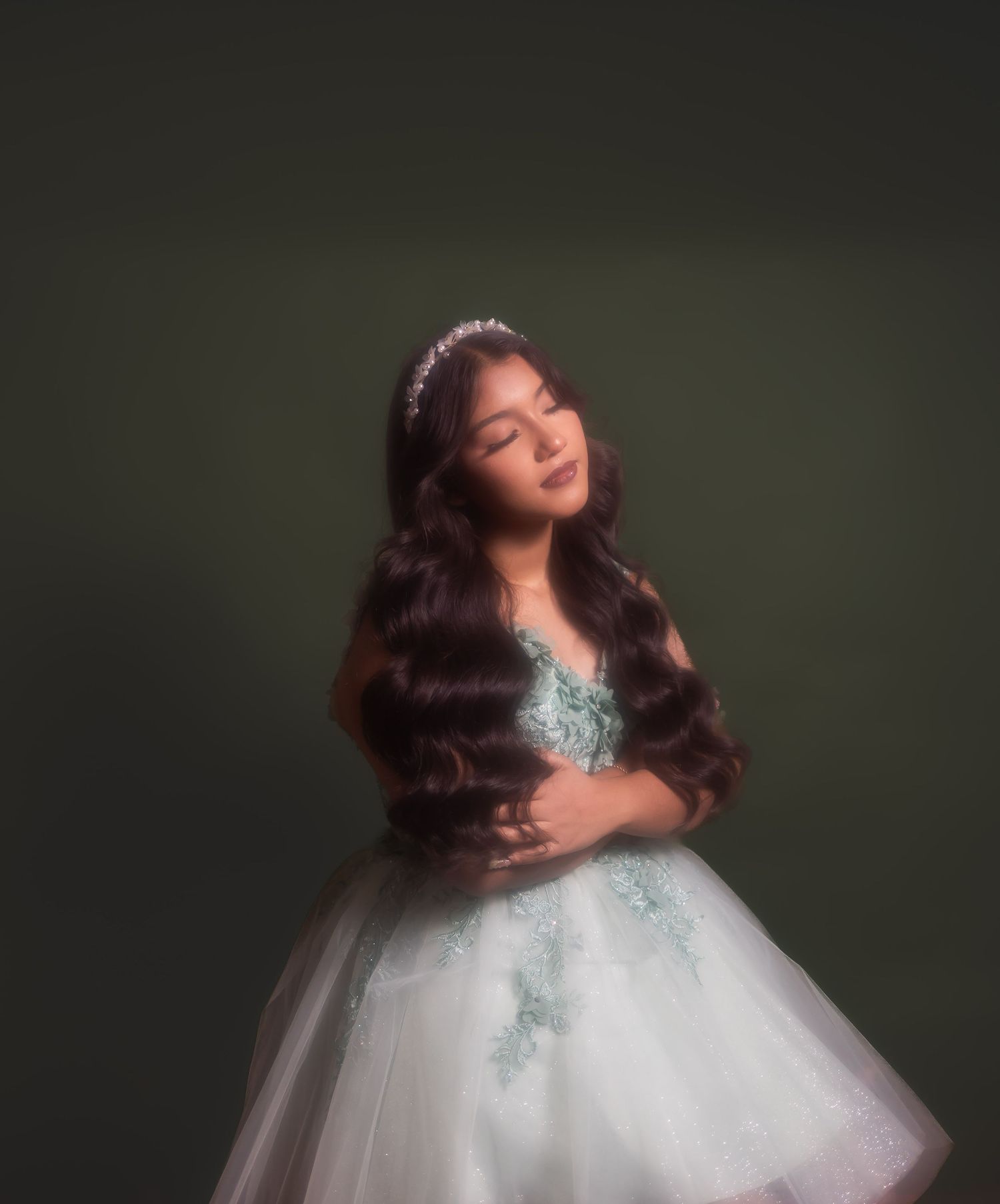 A woman in a white tulle gown with teal accents poses gracefully against a dark backdrop in a glamour portrait. Arizona studio