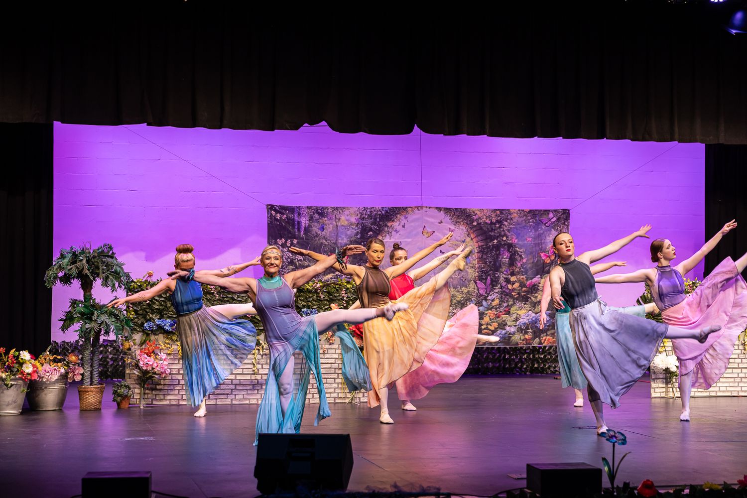 Dancers in flowing costumes perform on stage with purple lighting.