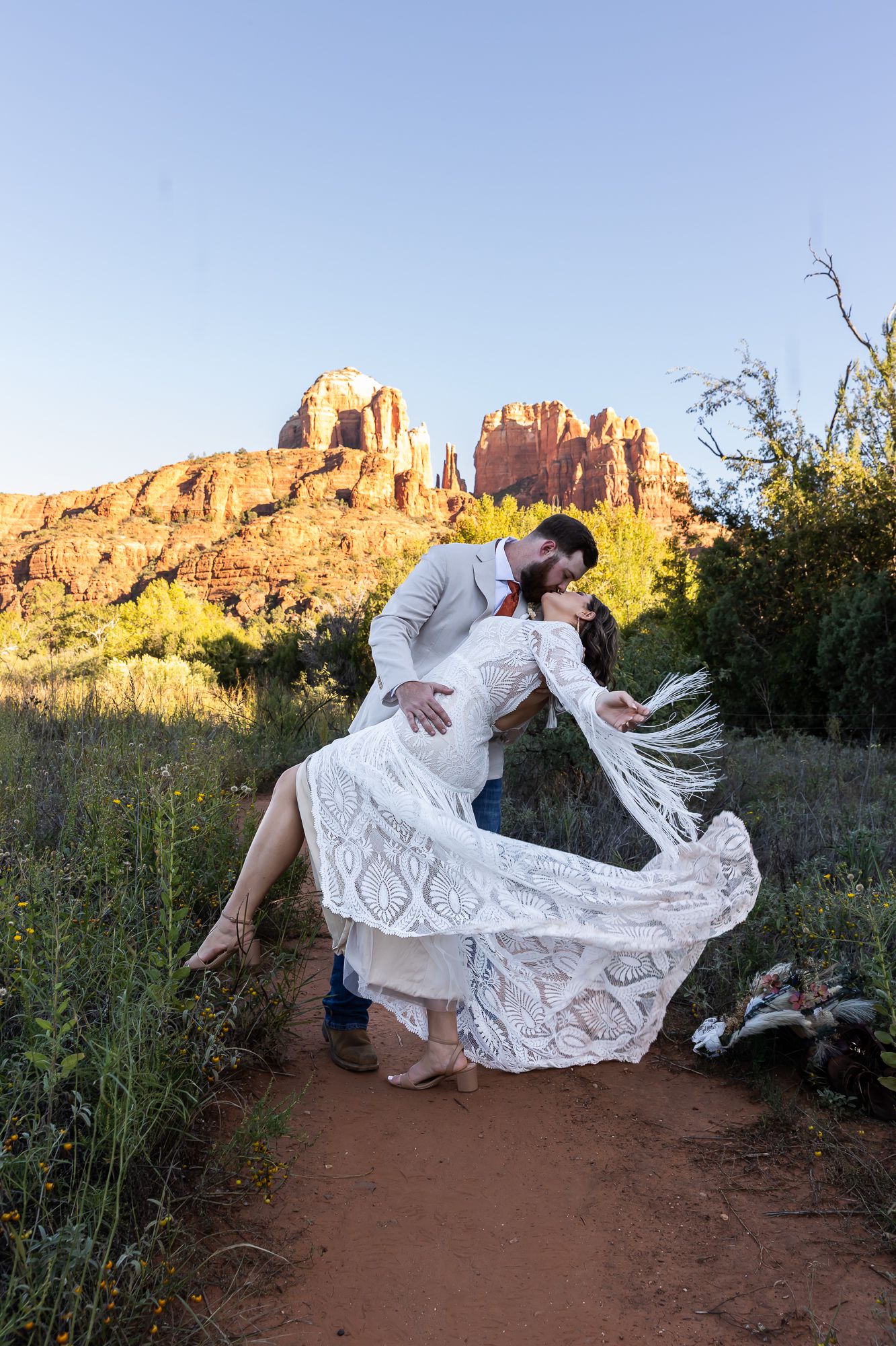 A romantic couple, wedding attire dips and poses dramatically on a desert trail with red rock formations at sunset. Sedona Arizona