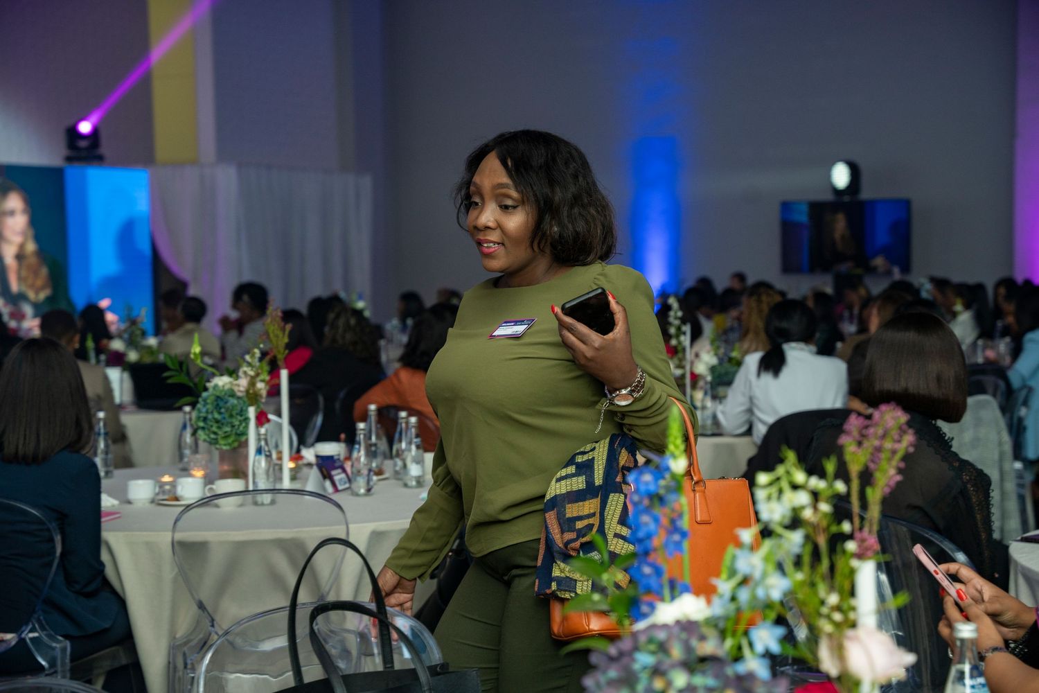 A woman in an olive dress holds a phone while networking at a formal Standard Bank conference.