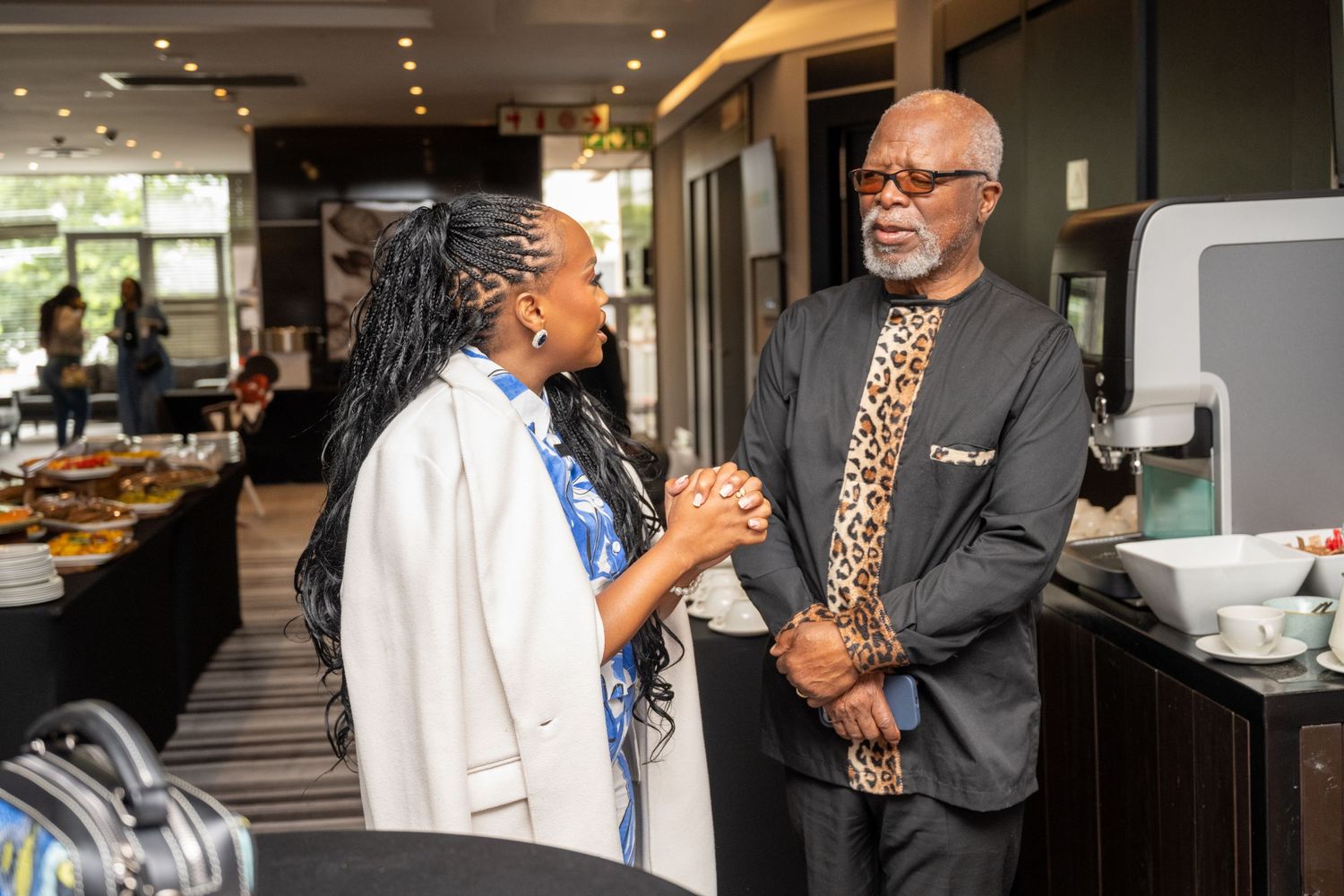 Two elegantly dressed people engaged in conversation at an upscale indoor event venue.