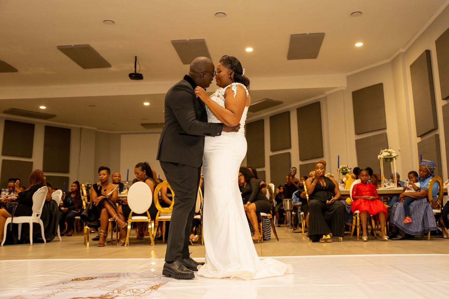 Bride and groom share romantic first dance at wedding reception with guests watching.
