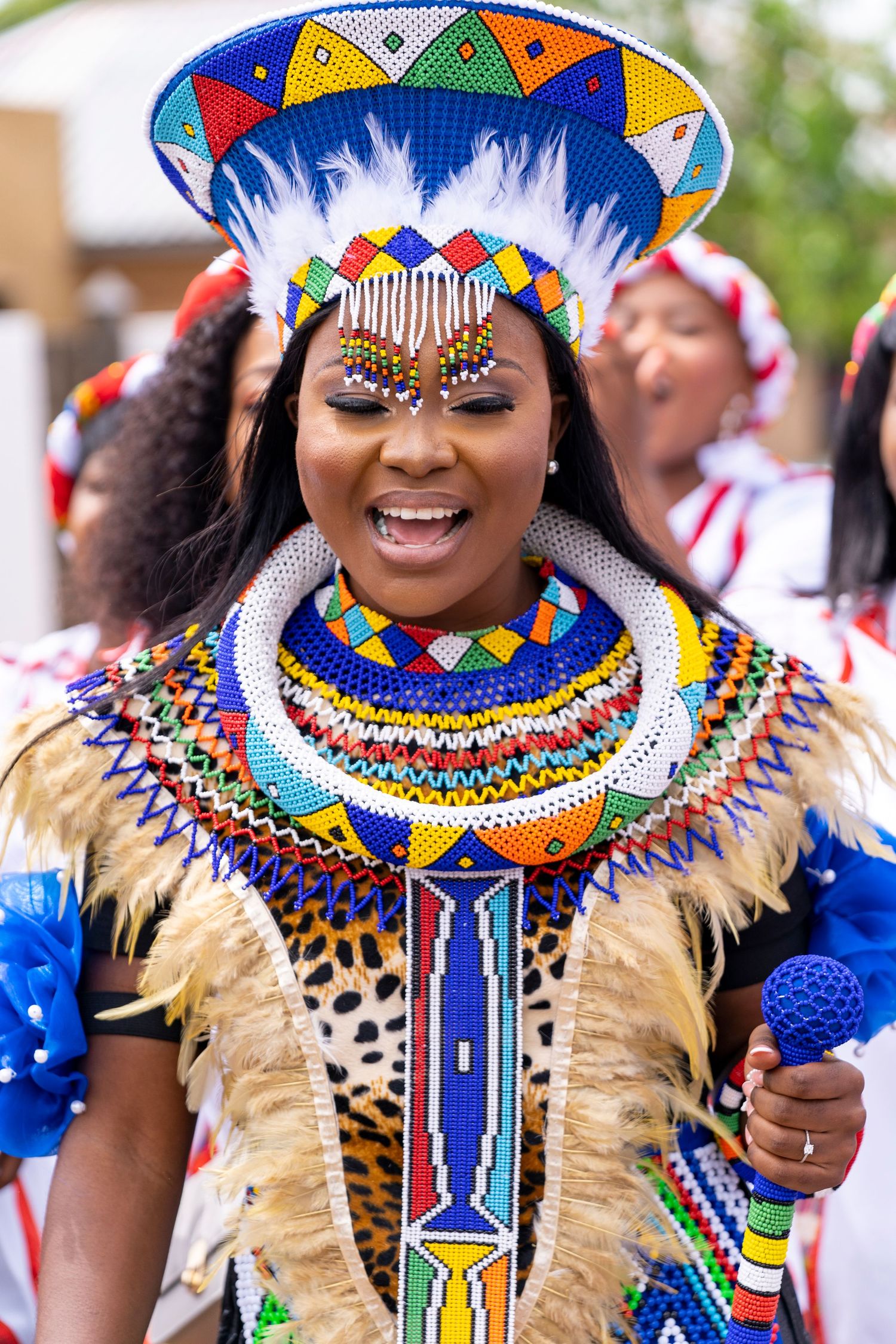 Smiling Zulu bride in elaborate colorful beaded headdress, necklace and leopard skin attire during traditional wedding.