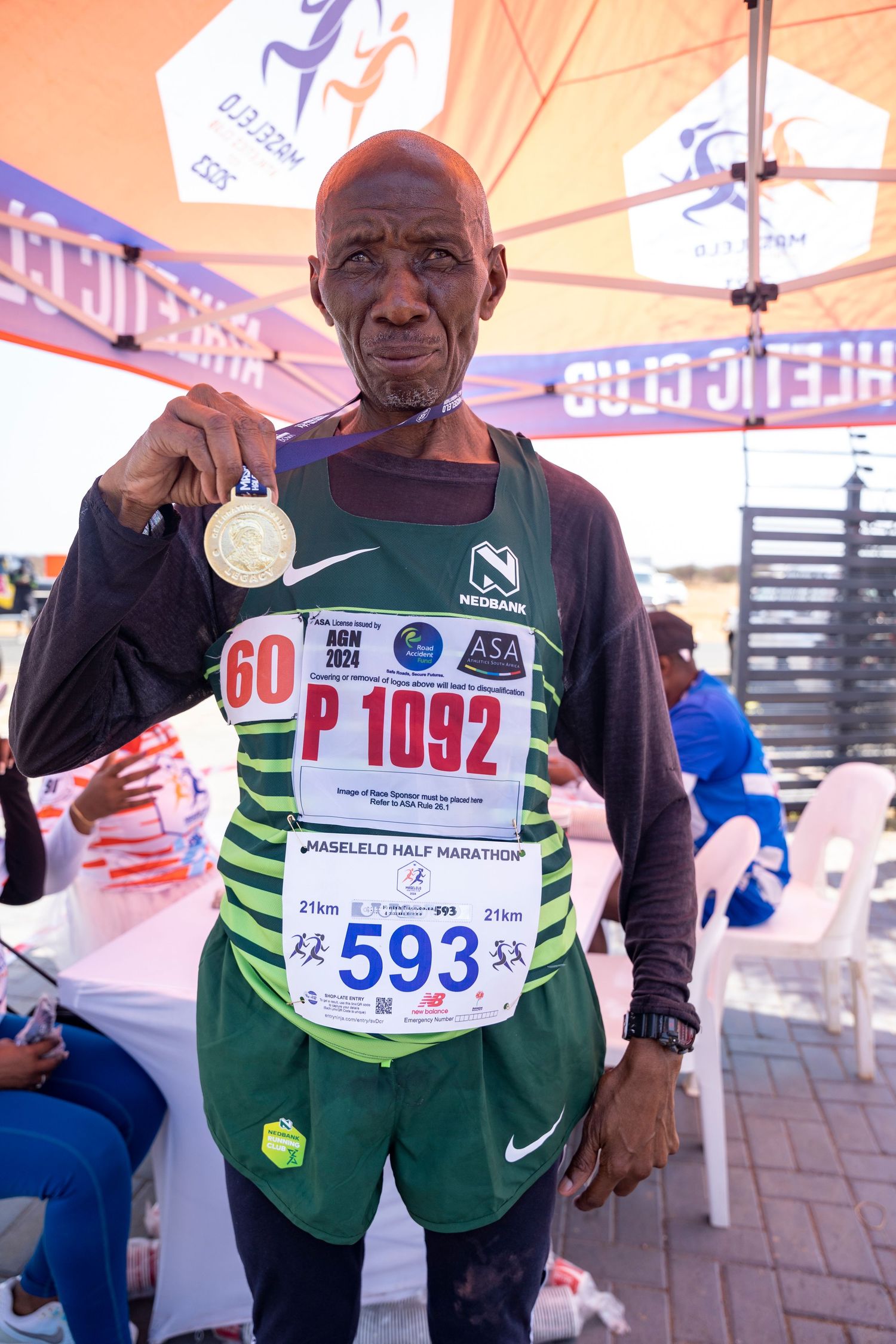 An elderly male runner proudly displays his gold medal at the Maselelo Half Marathon event.
