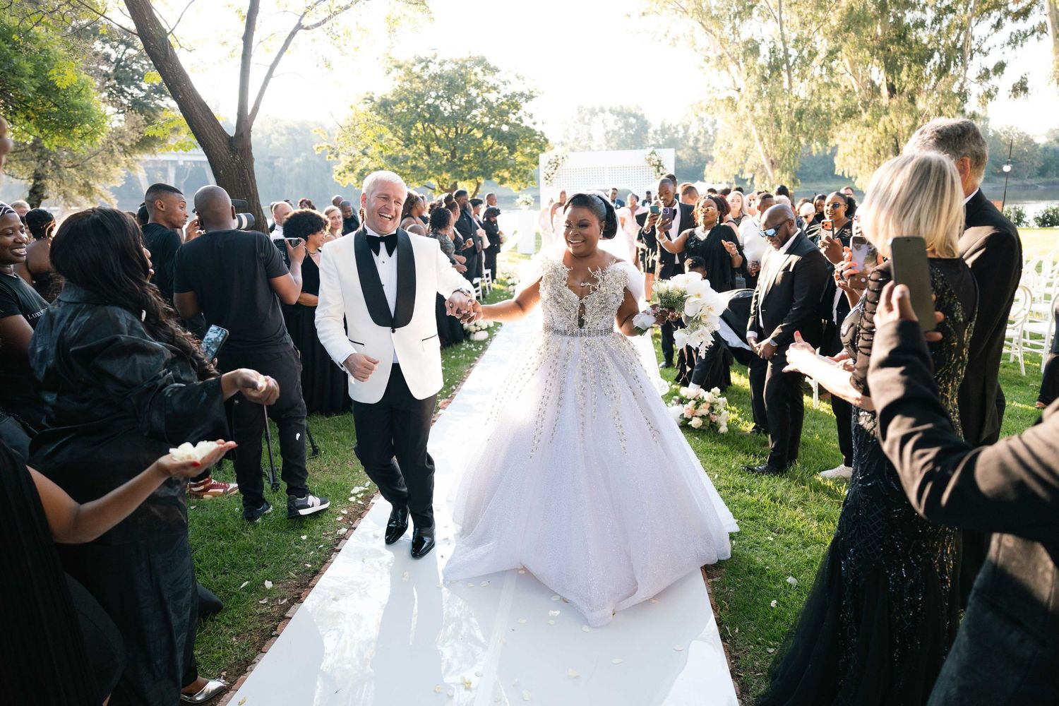 Newlyweds joyfully walk back down the aisle together after their outdoor wedding ceremony.