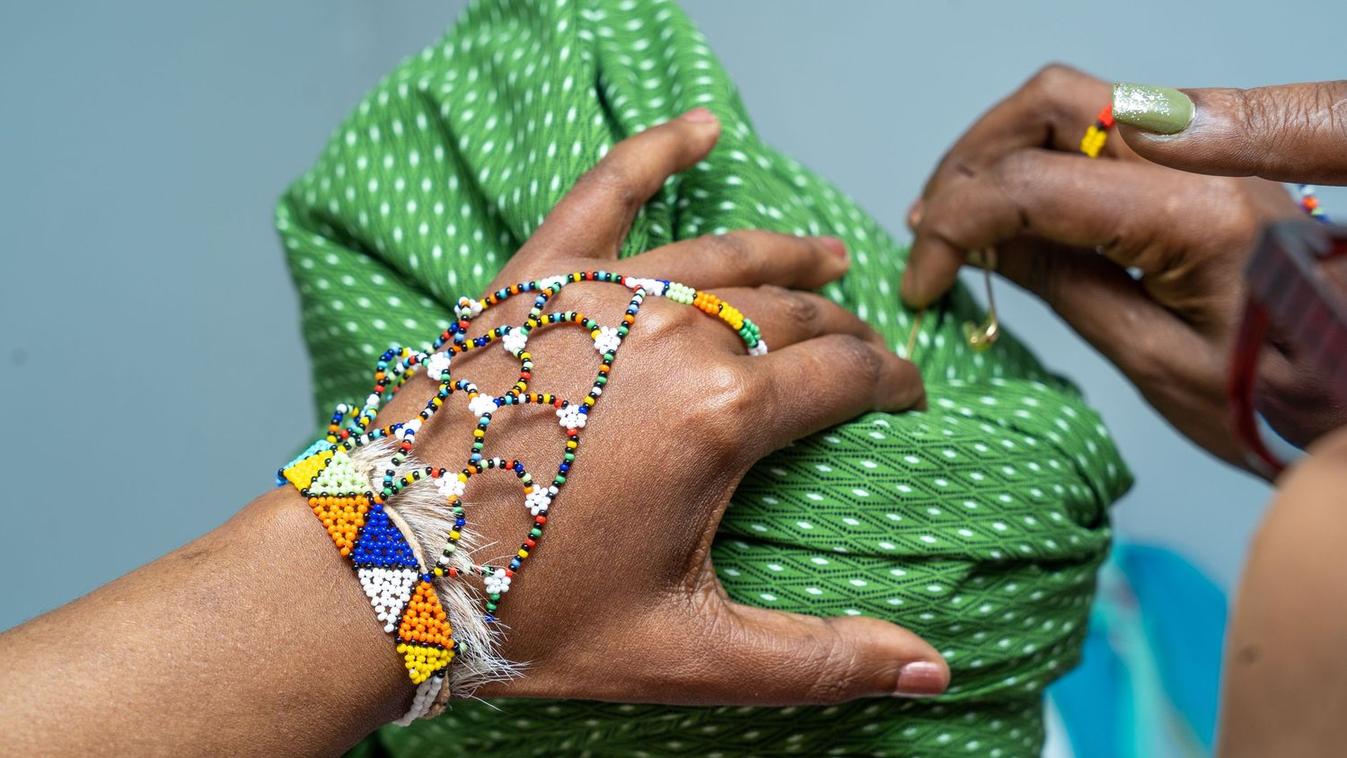 Close-up of hands adorned with colorful beaded African jewelry being fastened at a traditional ceremony.