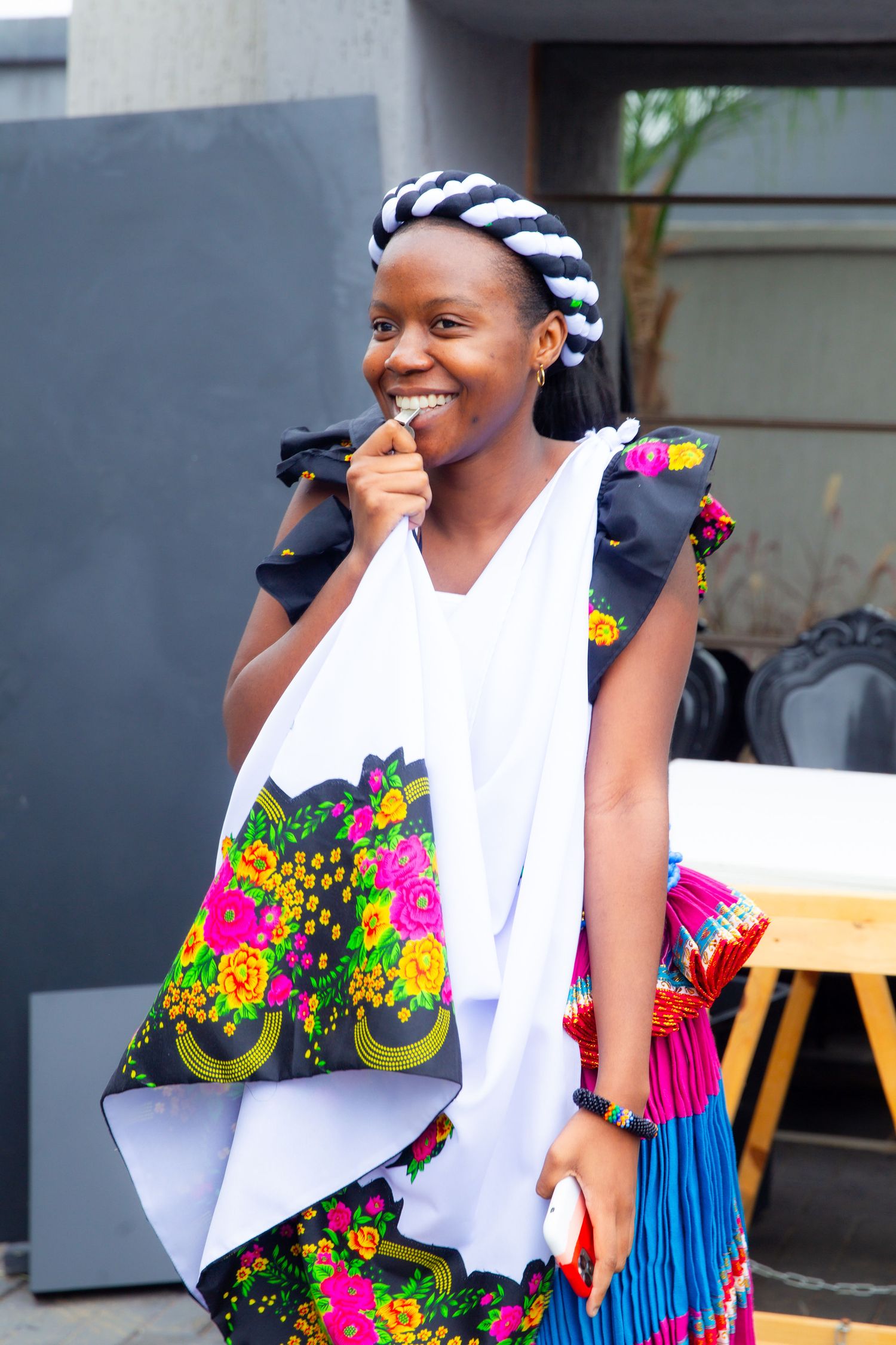 Smiling young woman in vibrant traditional African floral attire with black and white head wrap.