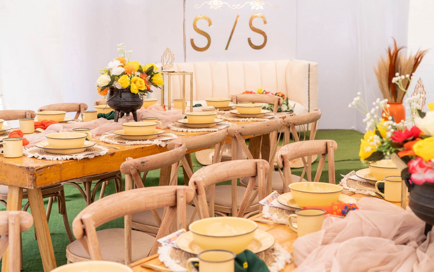 Rustic wedding reception table setup with wooden chairs, yellow plates, and floral centerpieces.