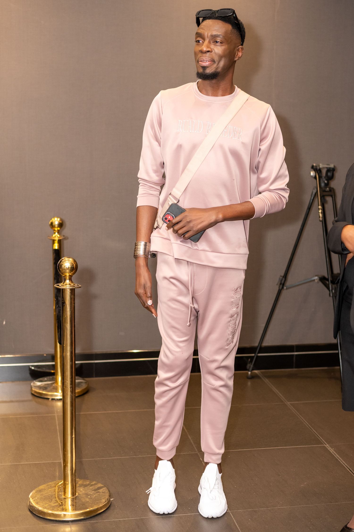 Young man in pink tracksuit with white sneakers posing at formal event entrance.