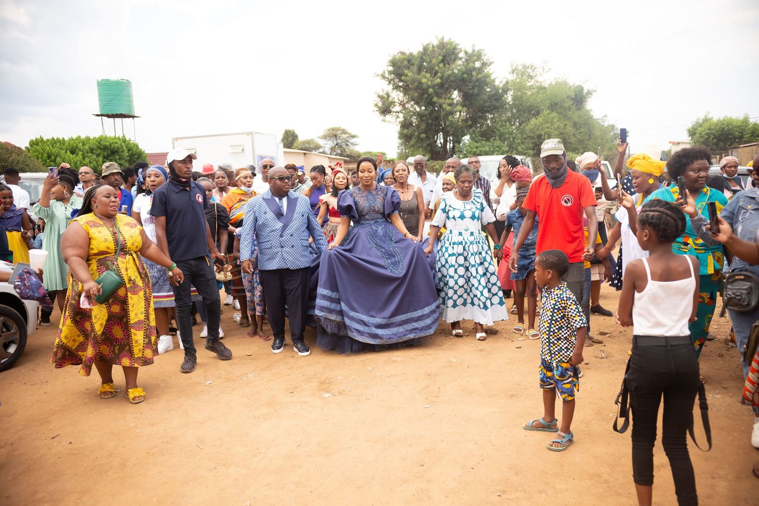 Group of people in colorful traditional African attire celebrating outdoors at a cultural wedding event.