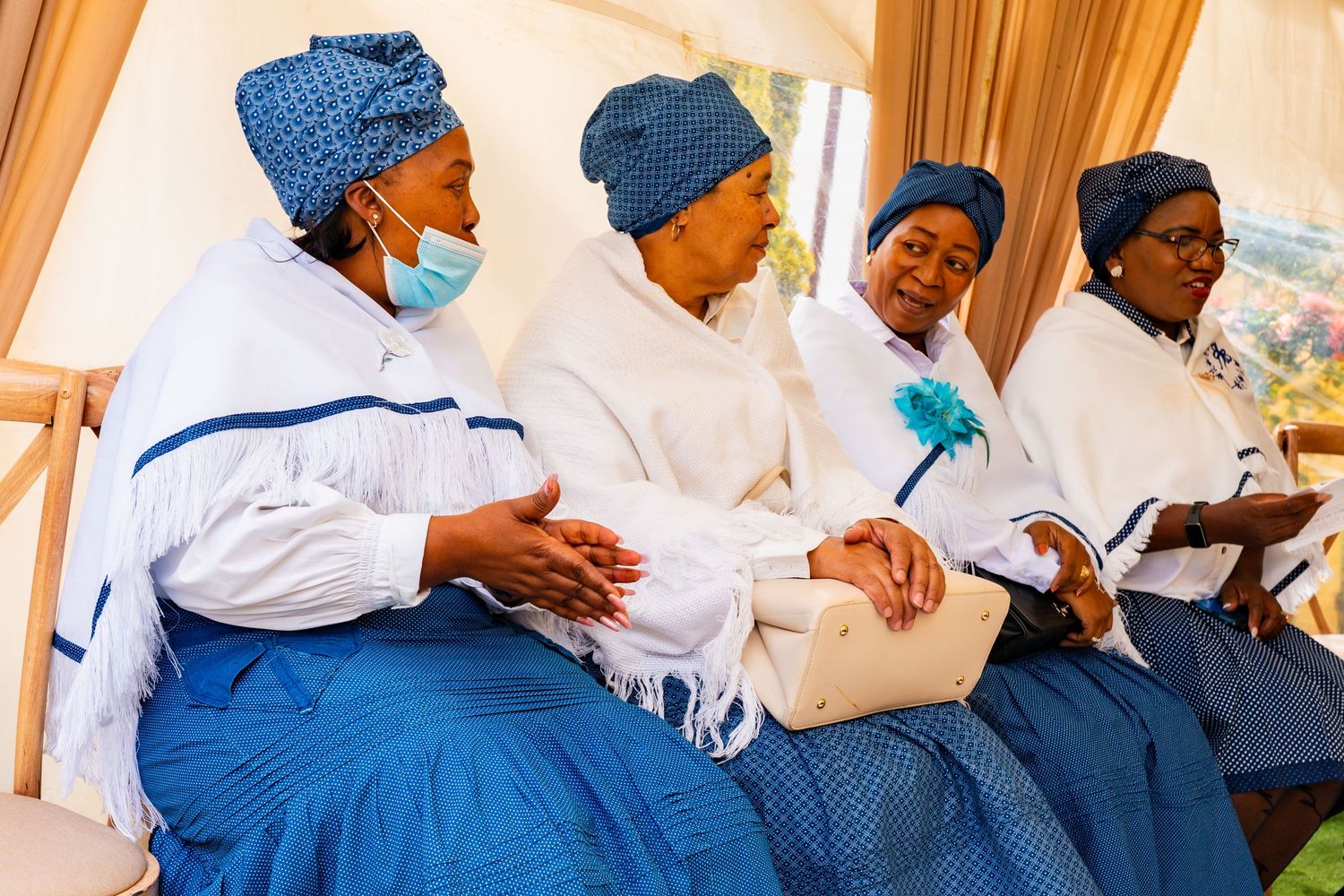 Four women in traditional blue and white attire sitting together at a cultural gathering.