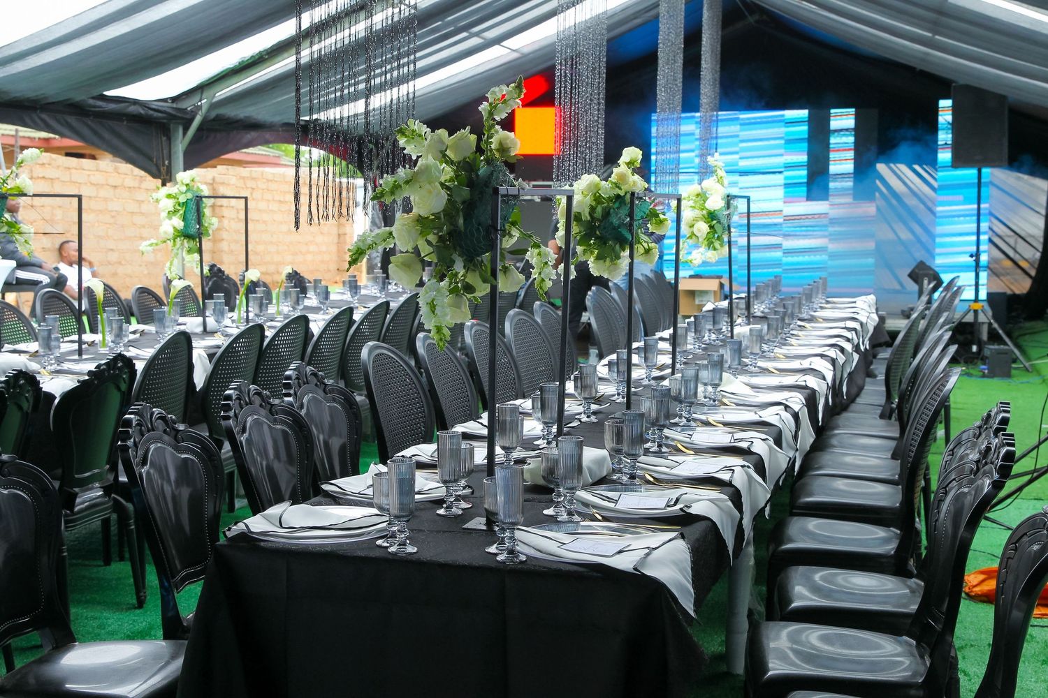 Elegant black-themed wedding reception setup with long tables, floral centerpieces, and black chairs under a marquee tent.